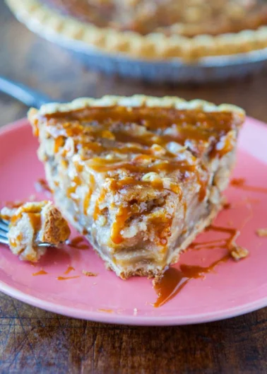 A slice of pie drizzled with caramel sauce on a pink plate with a fork containing a bite of the pie resting beside it.