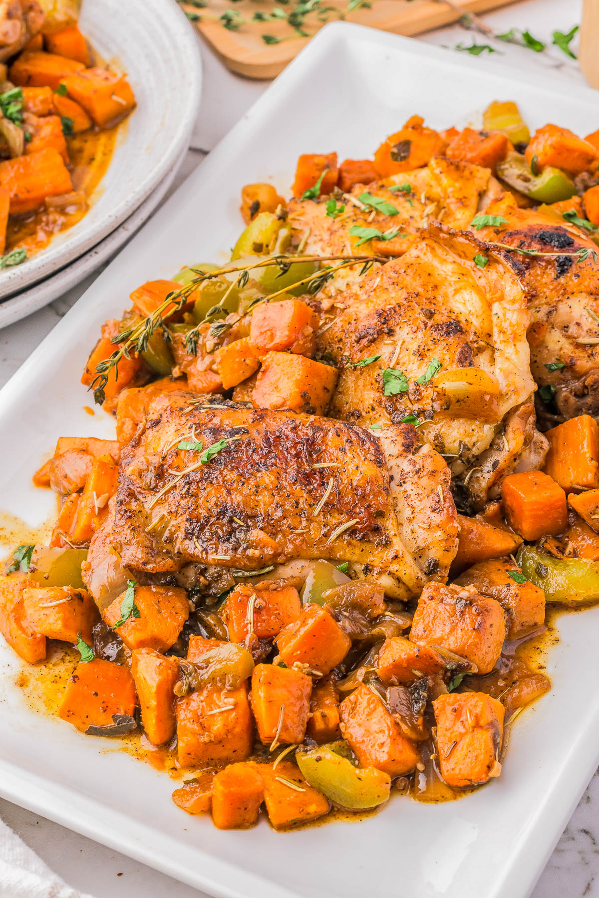 A plate of roasted chicken thighs garnished with herbs, served with diced sweet potatoes and vegetables in a savory sauce.