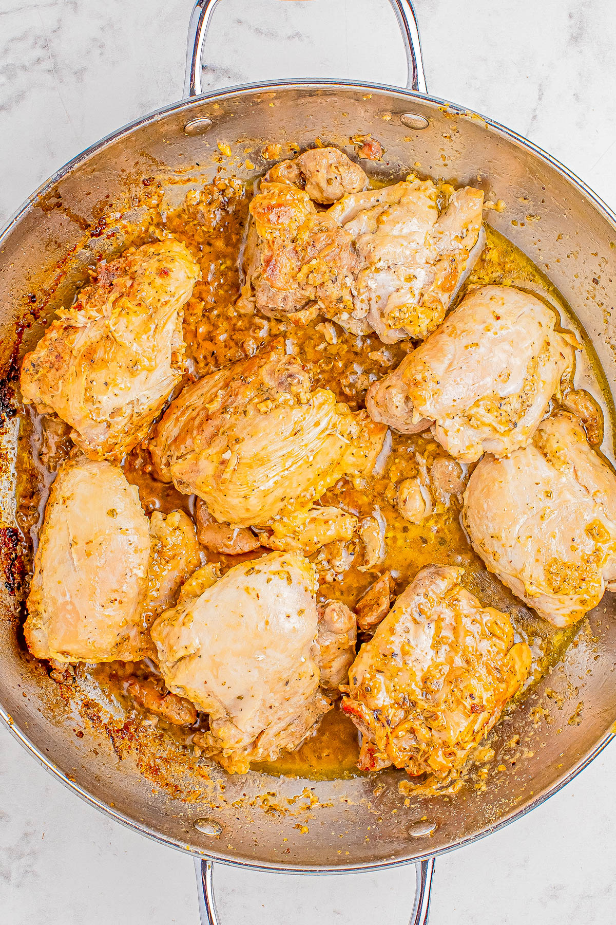 A stainless steel pan contains cooked, marinated chicken pieces with a yellowish-brown sauce.