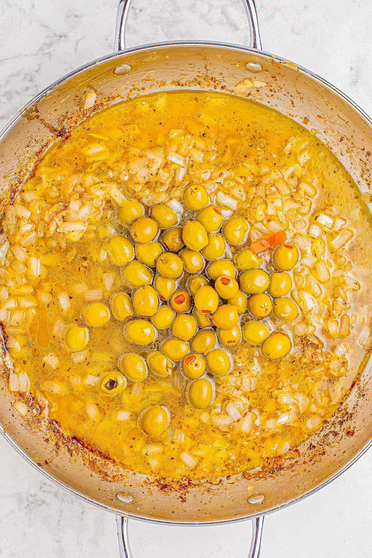 A pan filled with yellow curry sauce, chopped onions, and green olives.