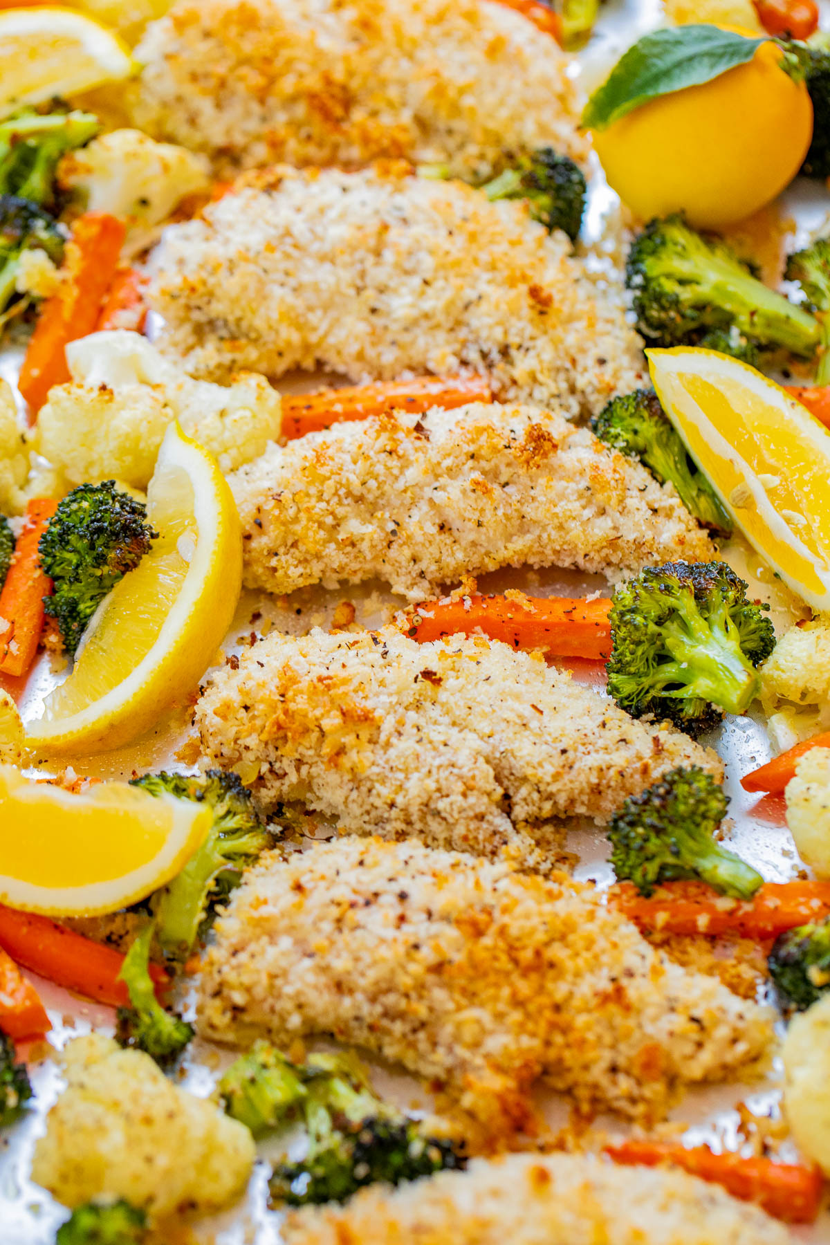 Breaded chicken fillets served with roasted broccoli, cauliflower, and carrot slices, garnished with lemon wedges.