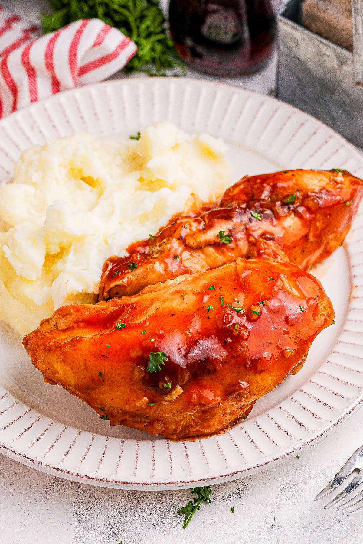 A plate with mashed potatoes and two pieces of glazed, seasoned chicken breast garnished with herbs.