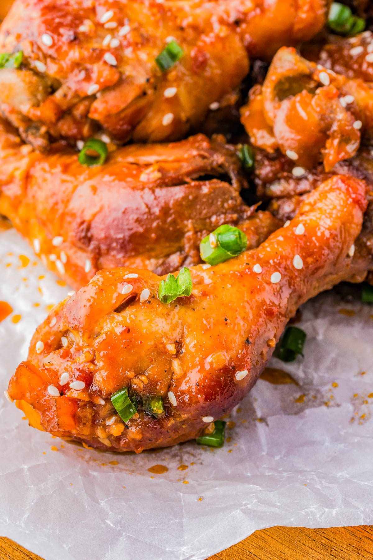 Close-up of glazed chicken drumsticks garnished with sesame seeds and chopped green onions on parchment paper.