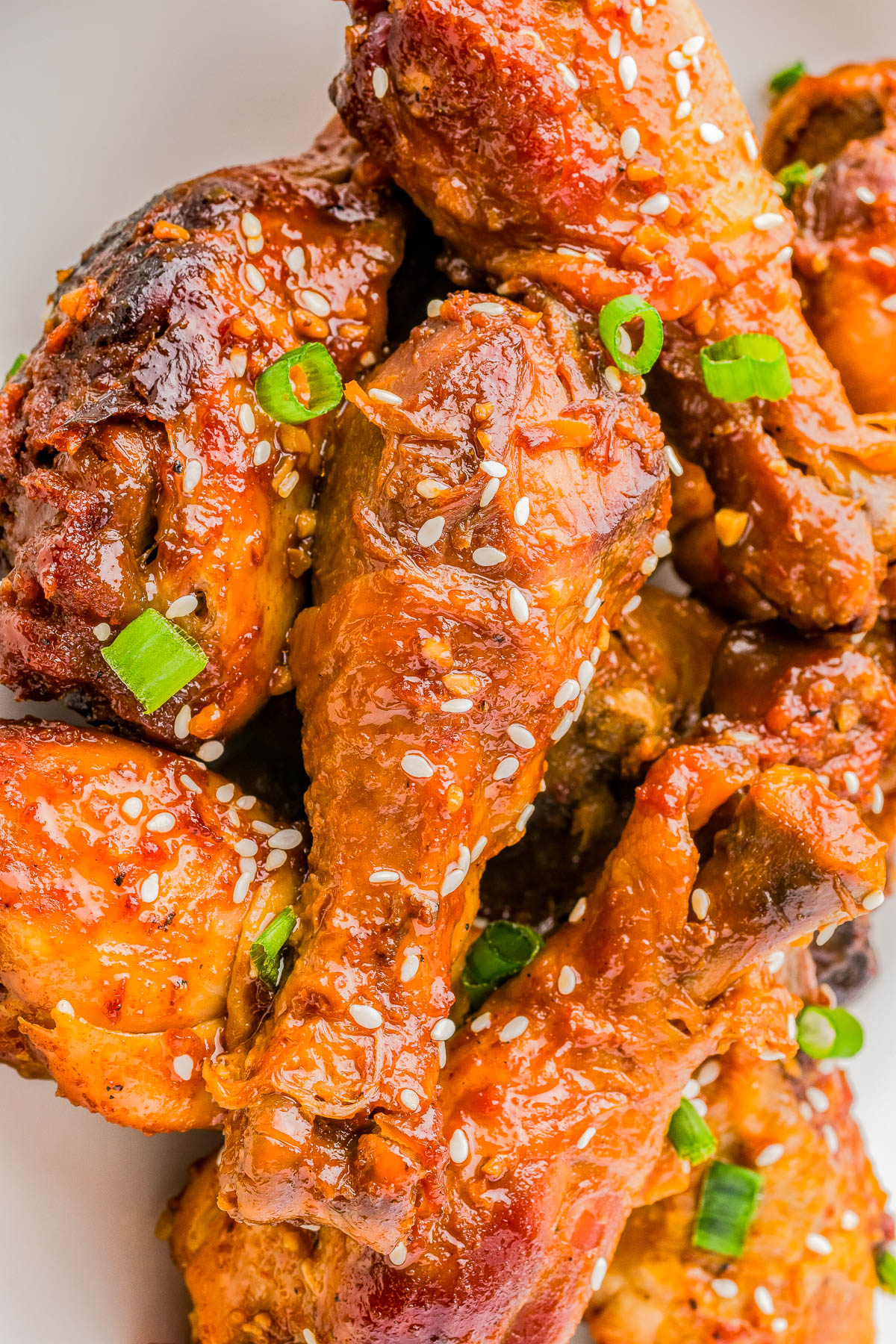 Close-up of glazed chicken drumsticks garnished with sesame seeds and chopped green onions.