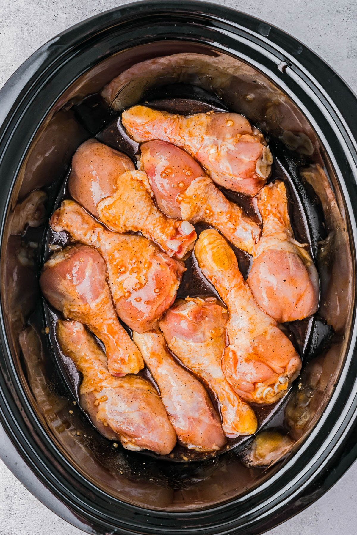 Raw marinated chicken drumsticks placed in a slow cooker, ready to be cooked.