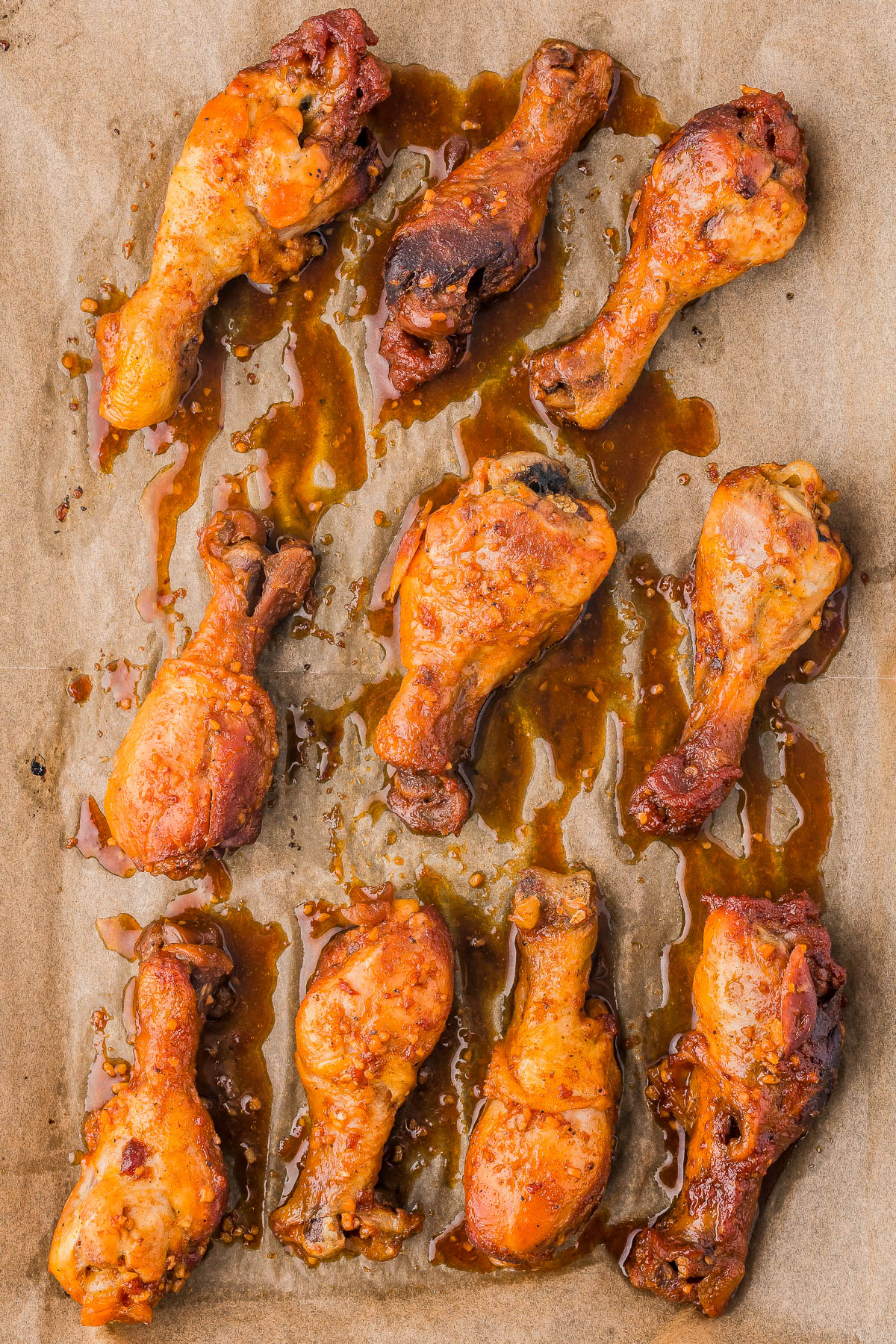 Ten cooked chicken drumsticks arranged on a parchment-lined baking tray with sauce drippings.