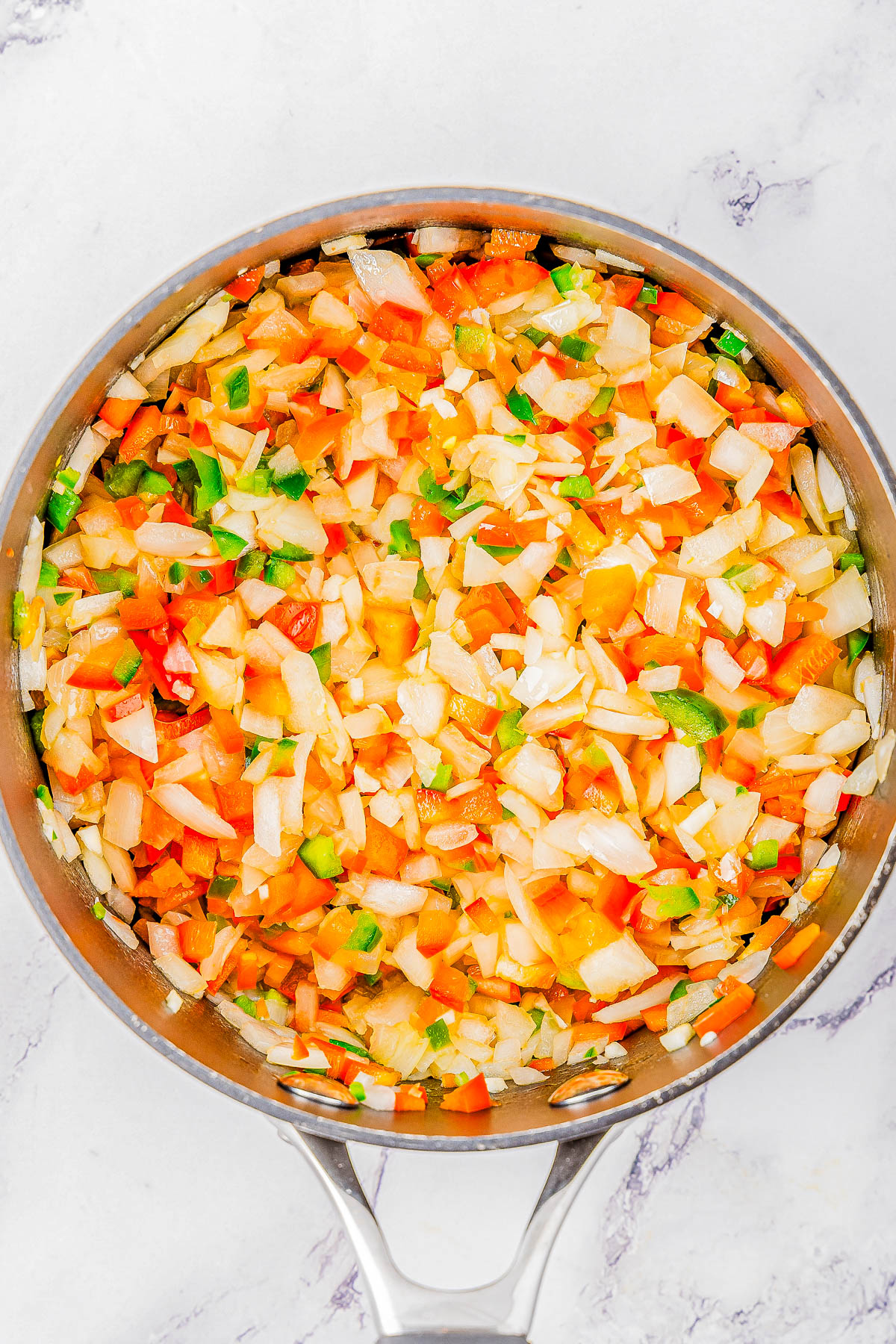 A metal pan filled with a colorful mix of chopped vegetables, including onions, bell peppers, and possibly other ingredients. The pan is placed on a white, marble-like surface.