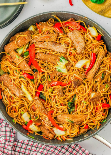 A stir-fry pan filled with beef lo mein, featuring noodles, beef strips, red bell pepper slices, and cabbage pieces.