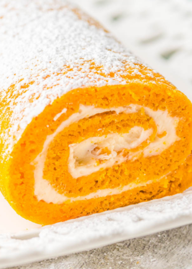 Close-up of a pumpkin roll cake with cream filling, dusted with powdered sugar on a white plate.