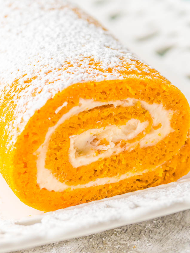 Close-up of a pumpkin roll cake with cream filling, dusted with powdered sugar on a white plate.