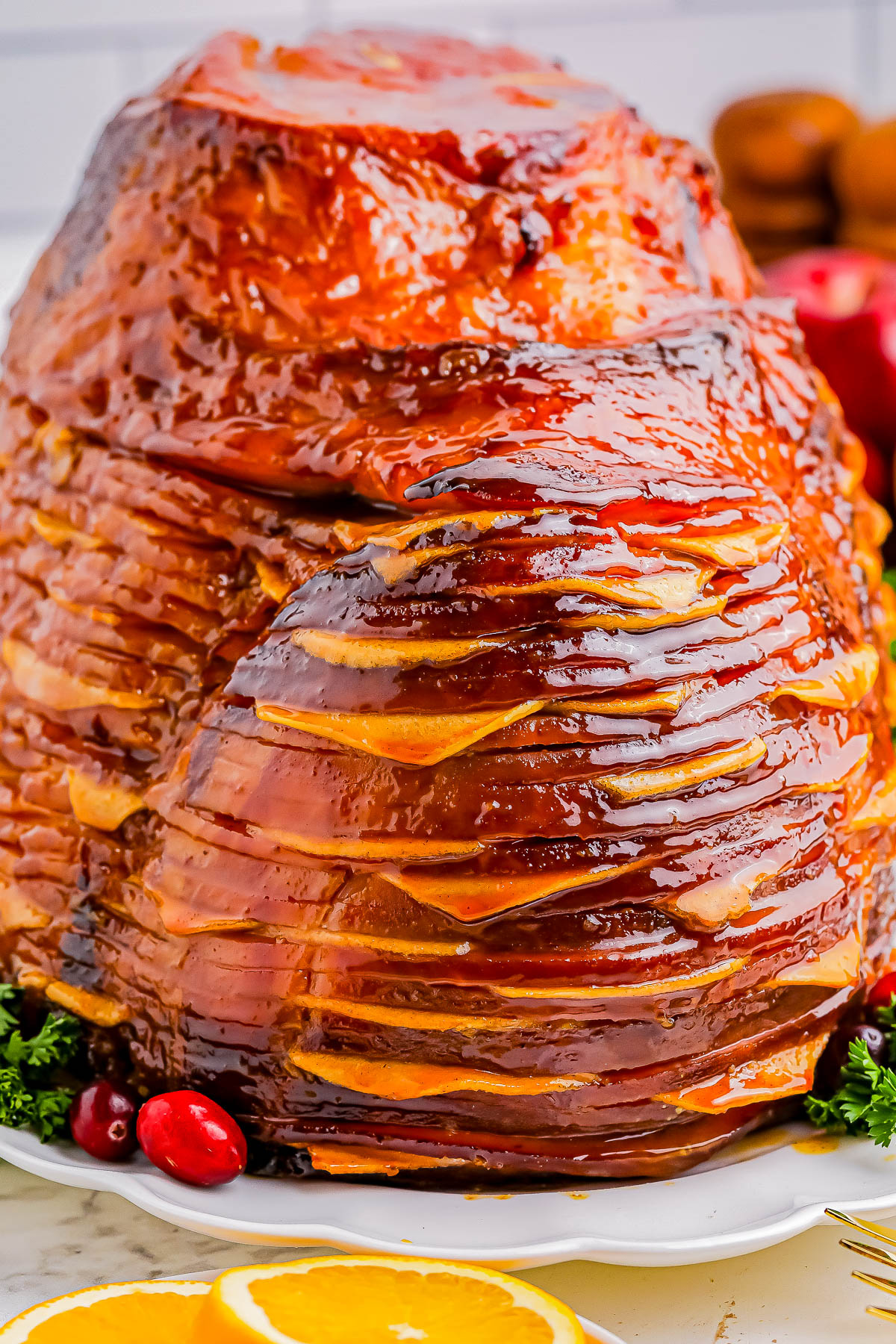 A glazed spiral-cut ham on a platter, garnished with oranges, cranberries, and parsley.