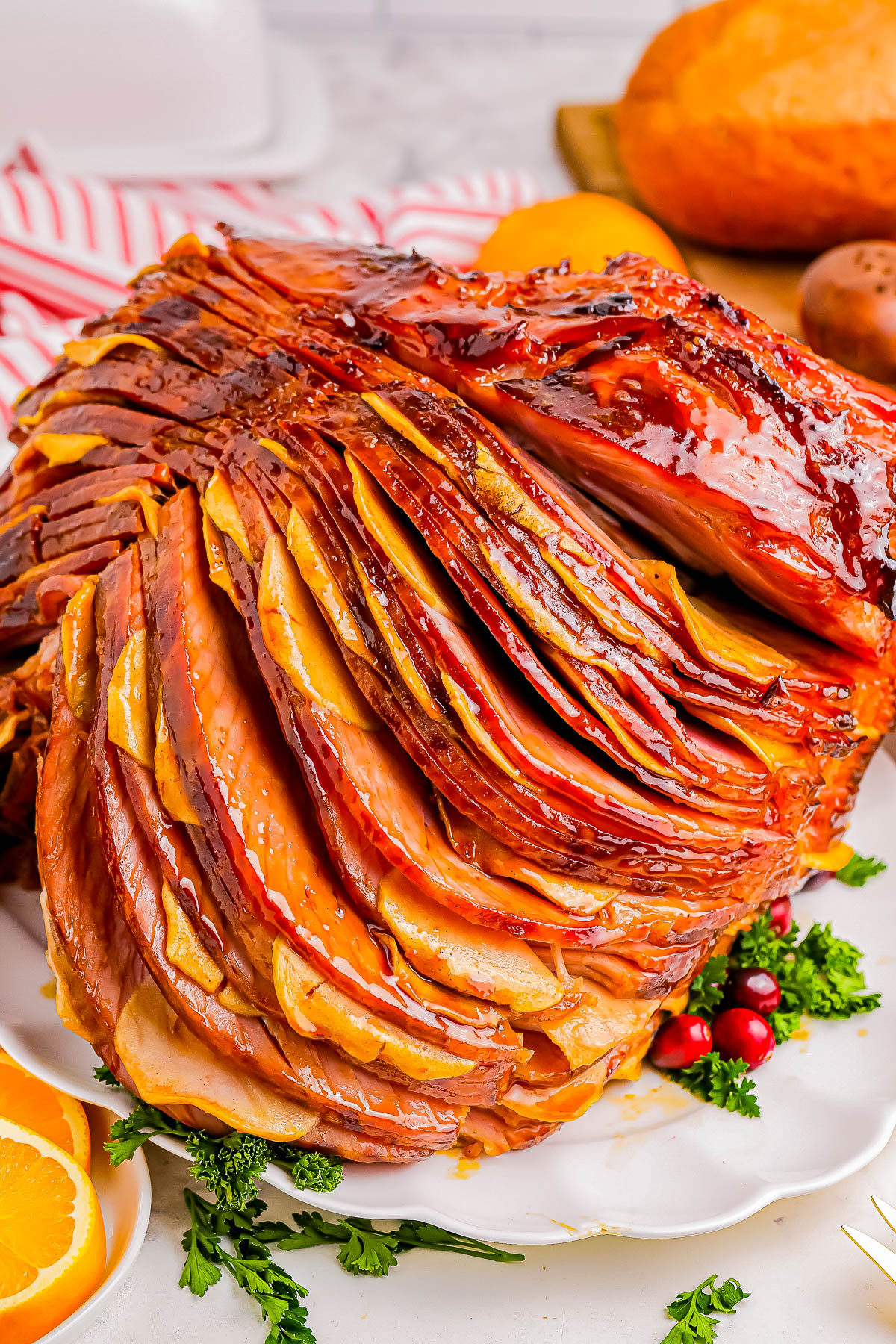 Glazed spiral-sliced ham garnished with herbs and cranberries on a white plate.