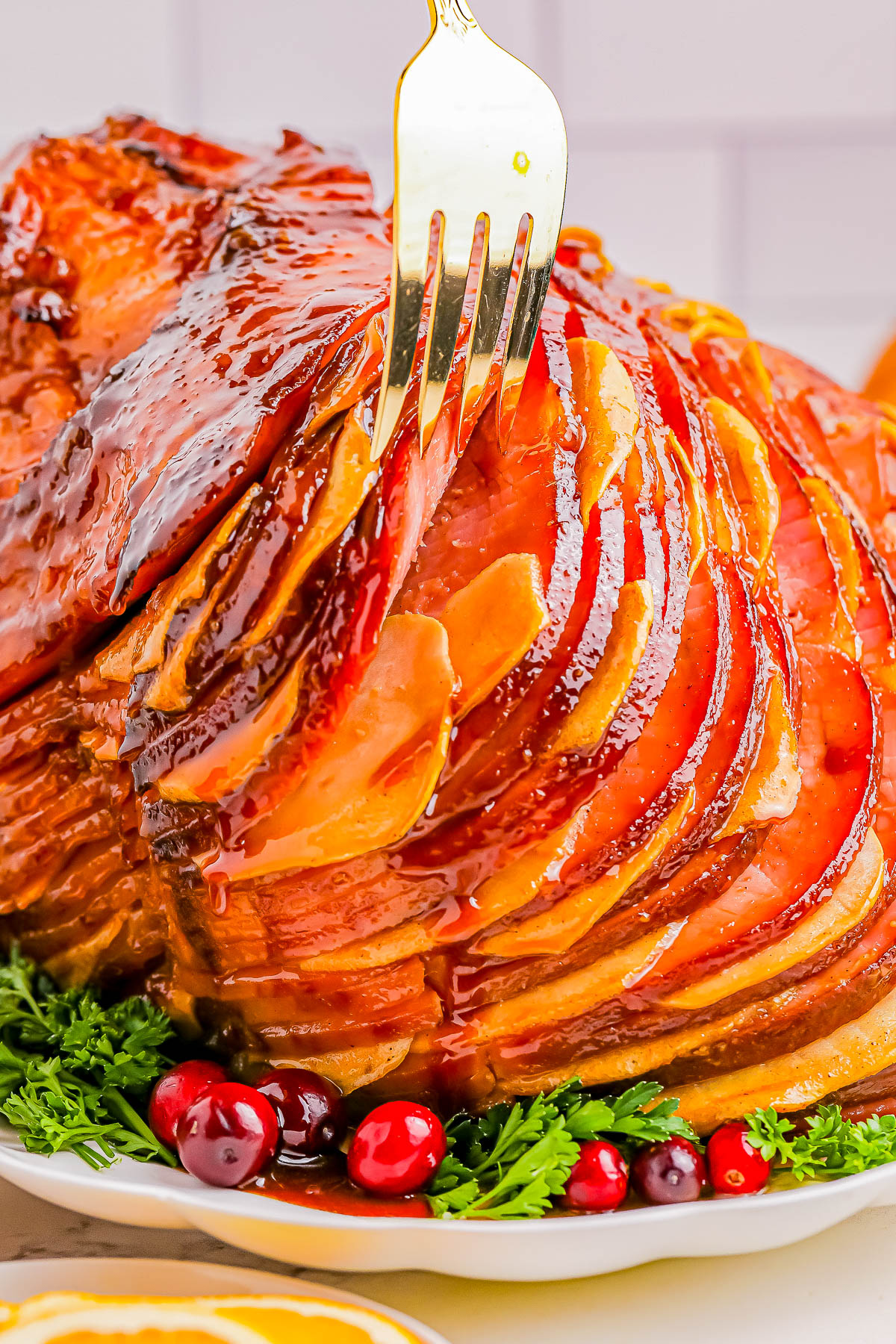 A fork inserted into a glazed, spiral-cut ham garnished with parsley and cranberries.