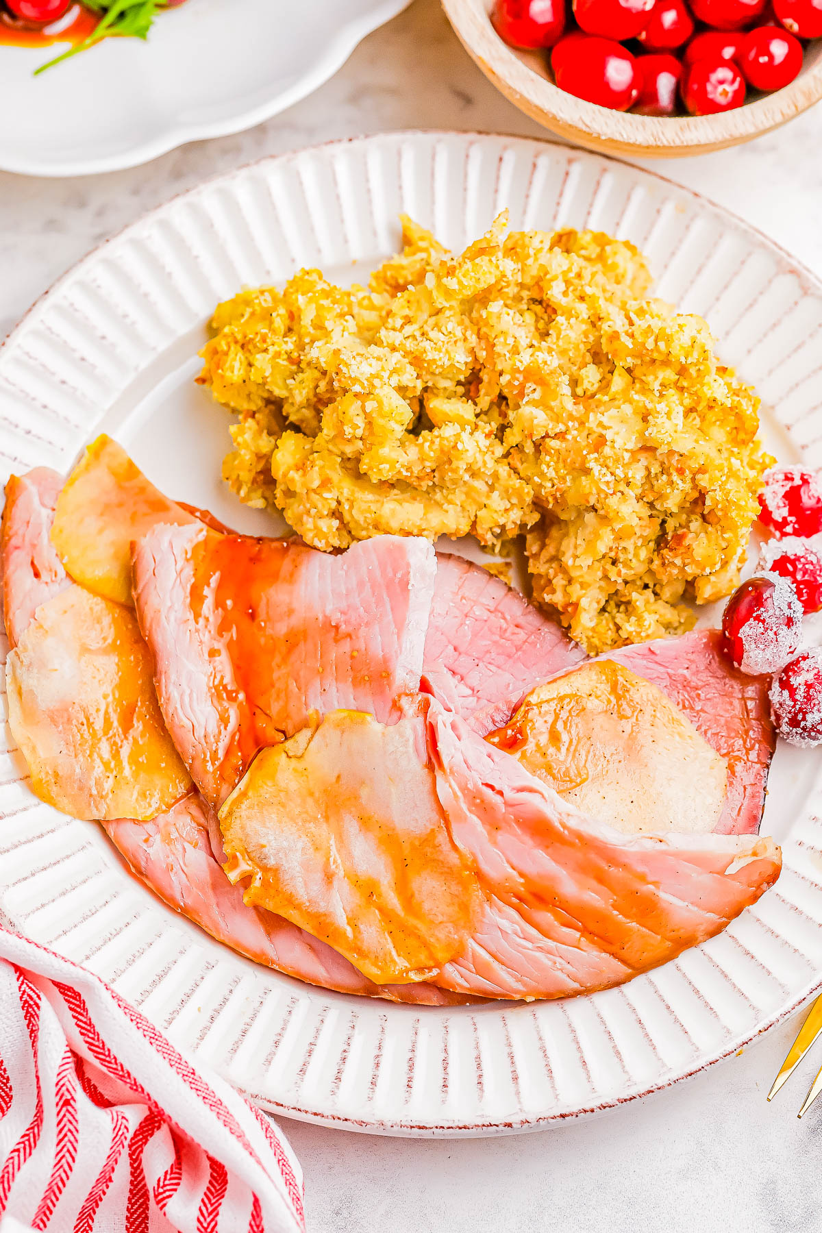 A plate with sliced ham, a serving of stuffing, and a few cherries.