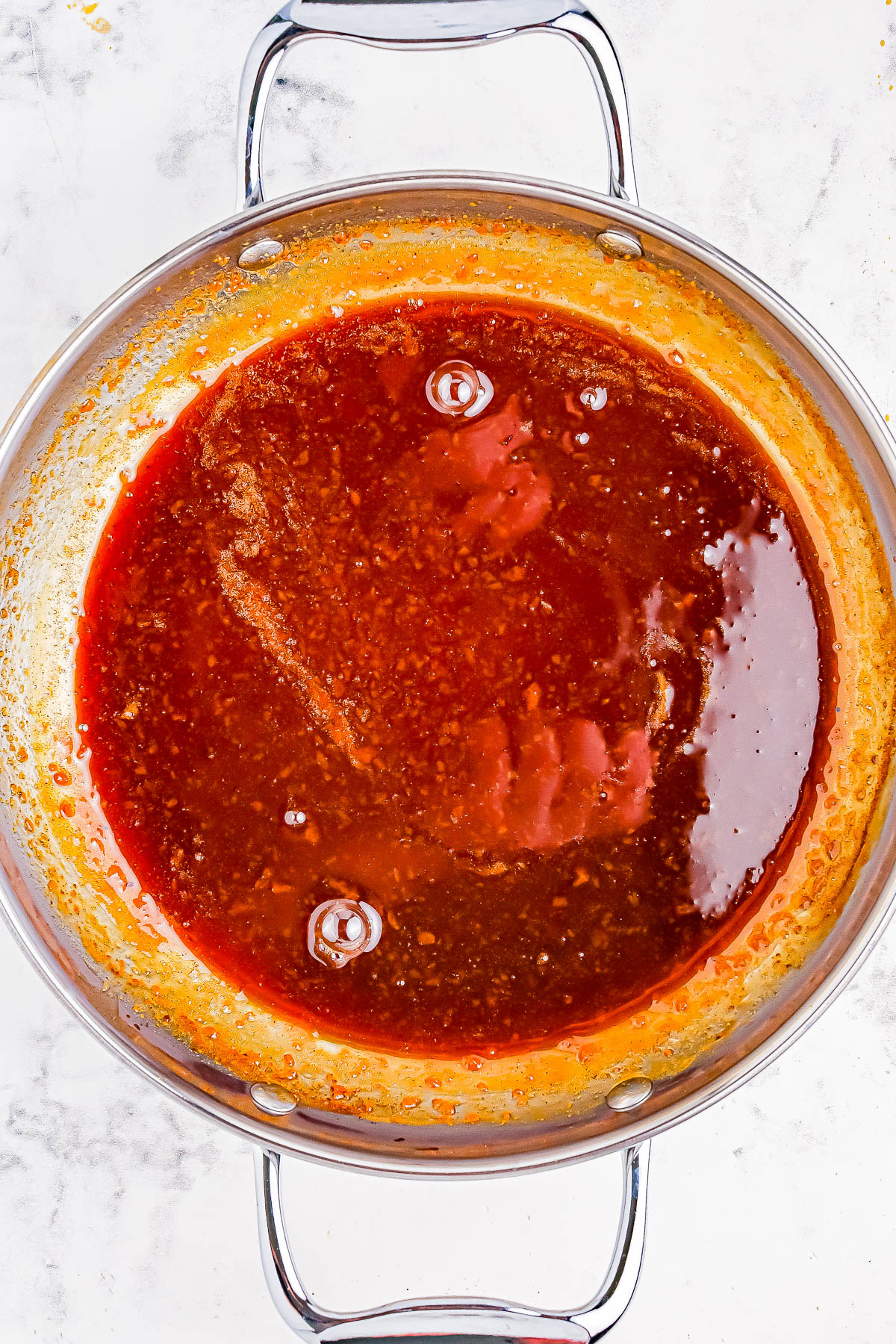 A stainless steel pan filled with a thick, red sauce on a light marble surface.