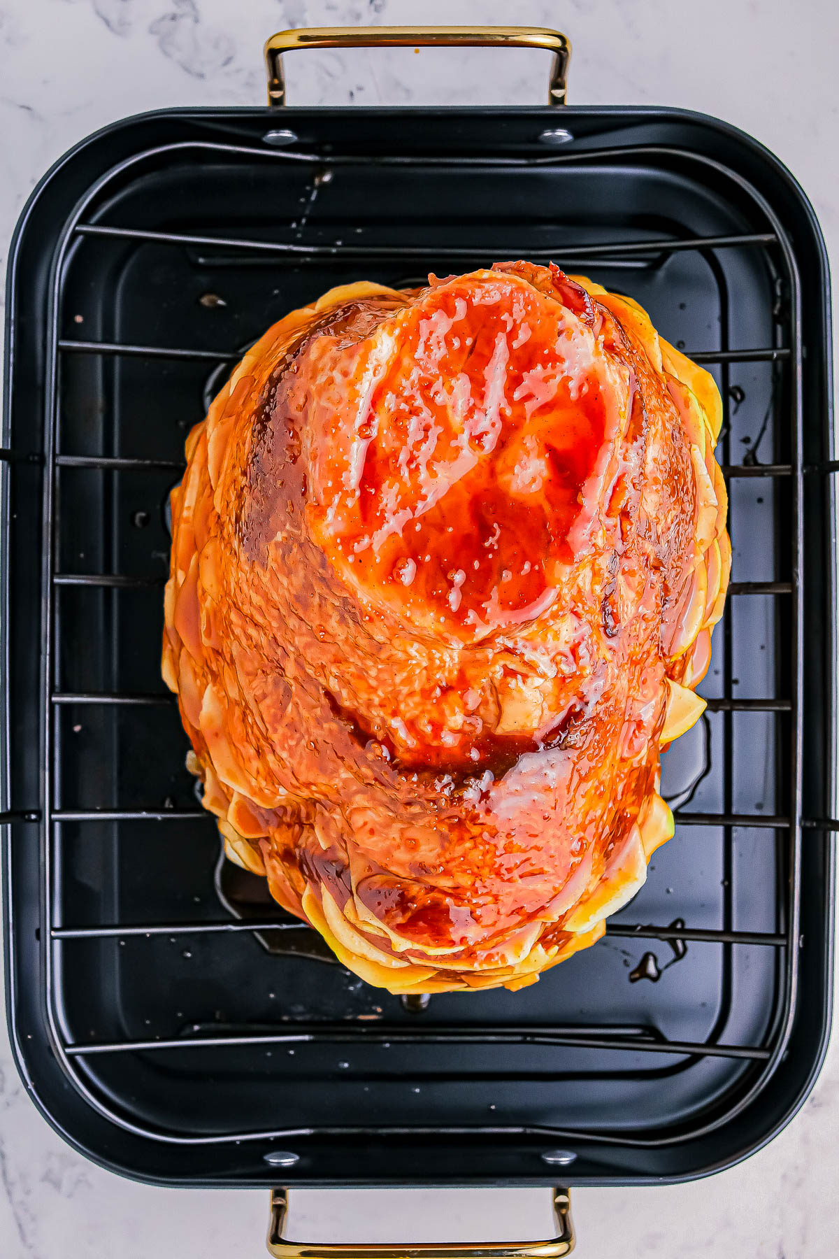 Roasted glazed ham on a black roasting rack set in a pan.