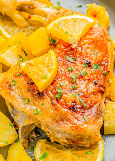 Roasted chicken with crispy skin, garnished with lemon slices and herbs, surrounded by roasted potato chunks.