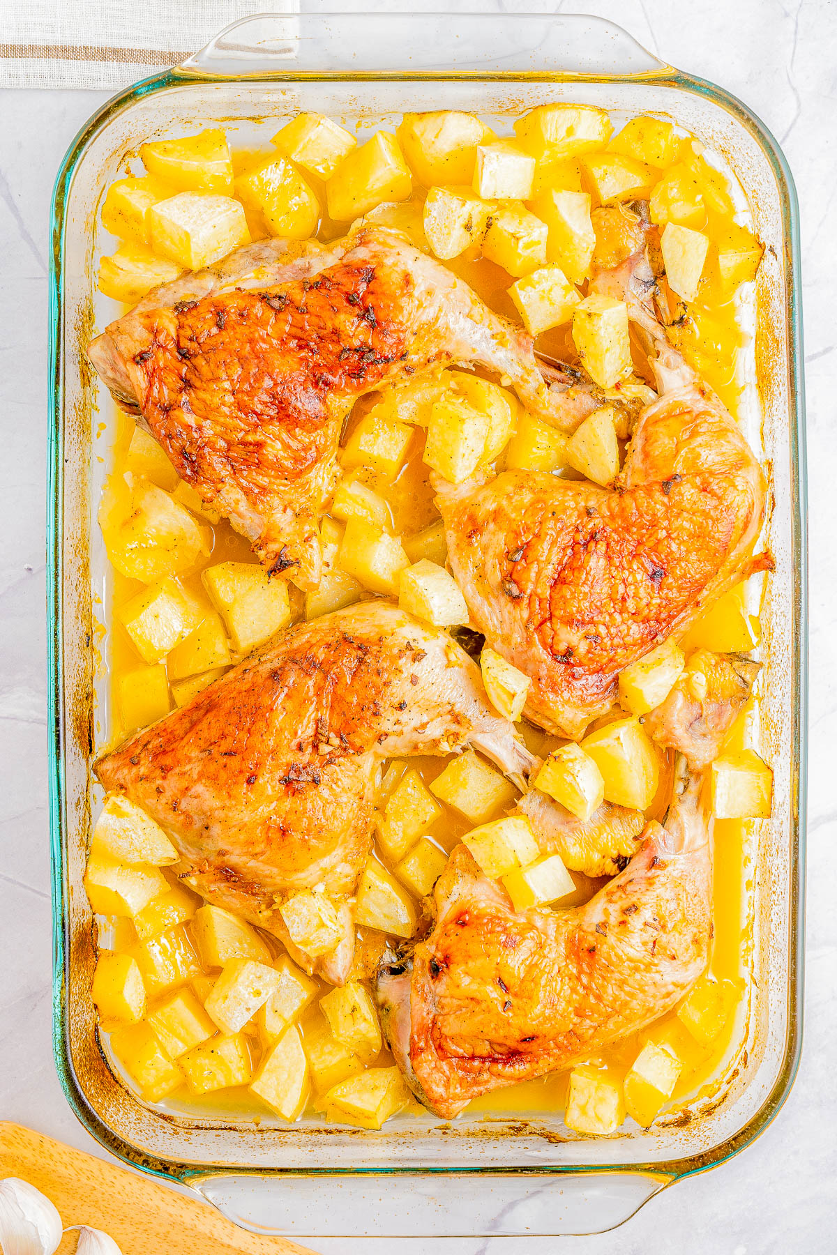 Baked chicken thighs and diced potatoes in a glass dish.