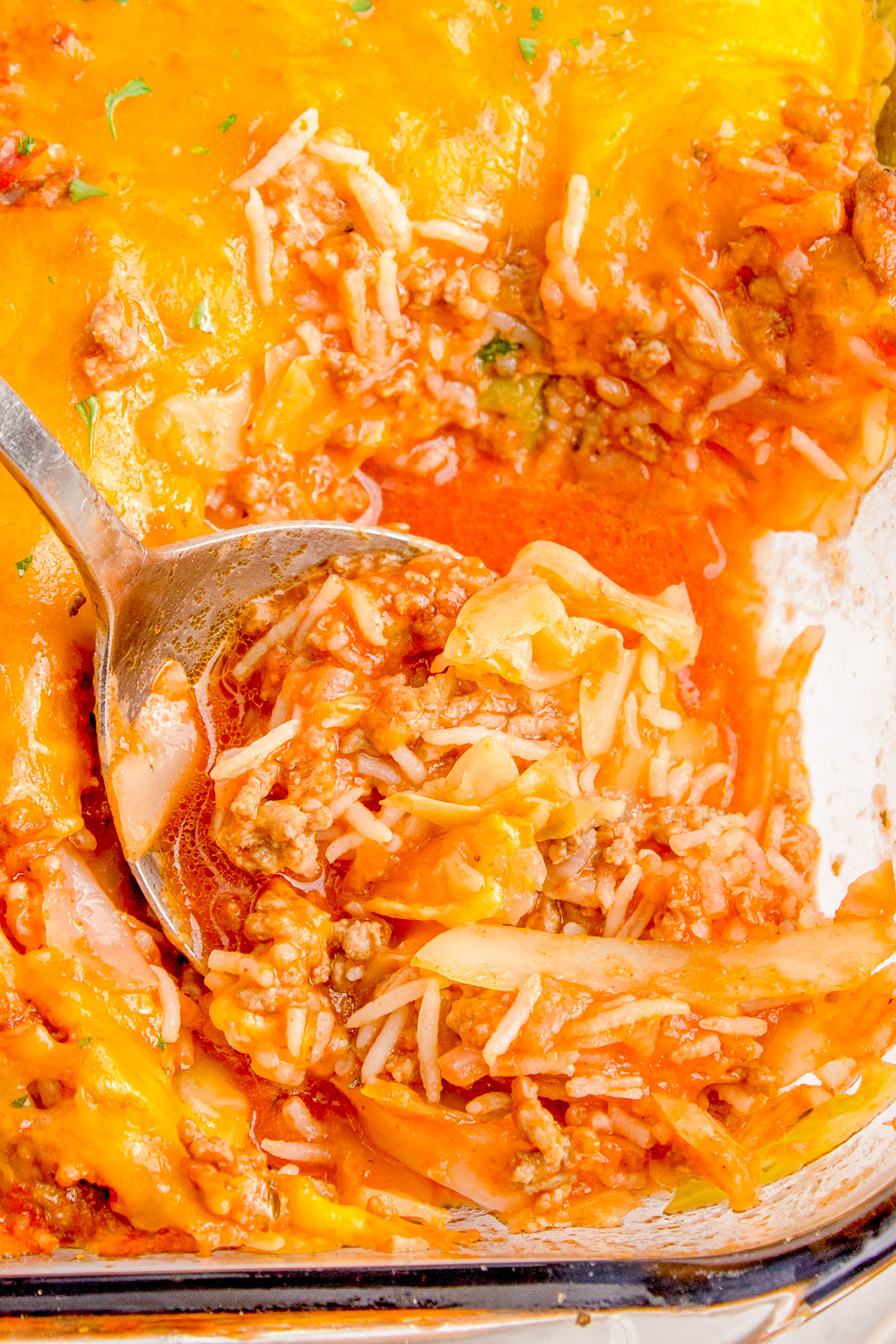 A close-up of a baked casserole with ground meat, tomato sauce, cheese, and pasta, with a spoon lifting some from the dish.