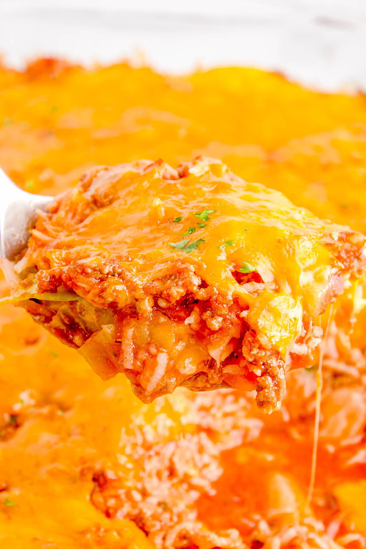 A close-up of a serving of cheesy, baked lasagna being lifted from a dish. The layers of pasta, meat sauce, and melted cheese are visible.