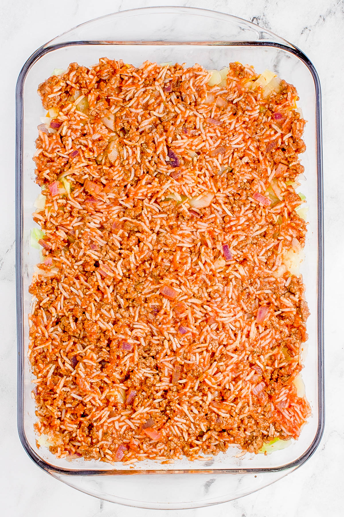 Glass dish filled with a layered casserole of rice, meat, and tomato sauce.