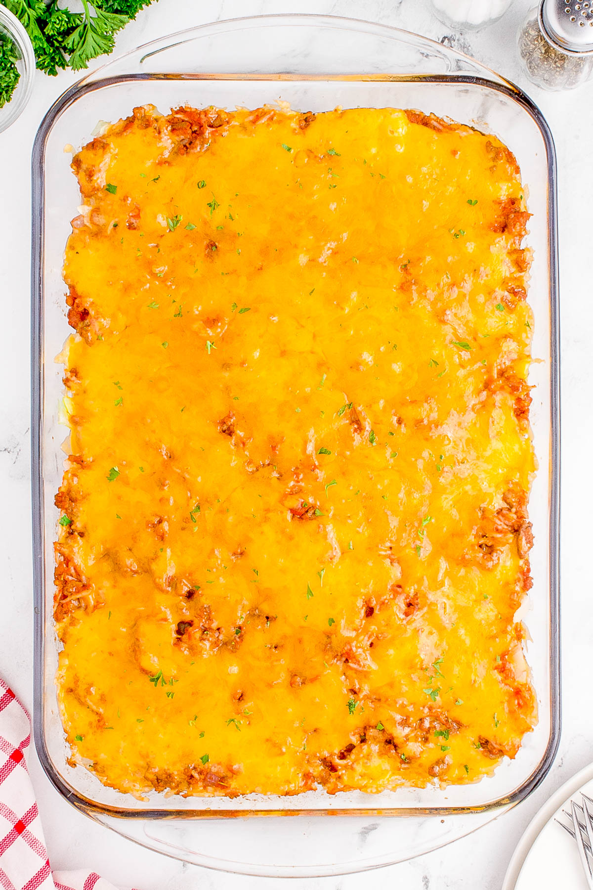 A glass baking dish filled with a golden-brown, cheesy casserole on a marble countertop.