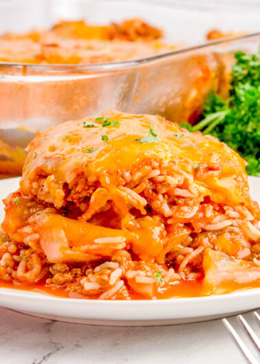 Close-up of a plate with a serving of cheesy beef and rice casserole, garnished with parsley. A glass baking dish with more casserole is visible in the background.