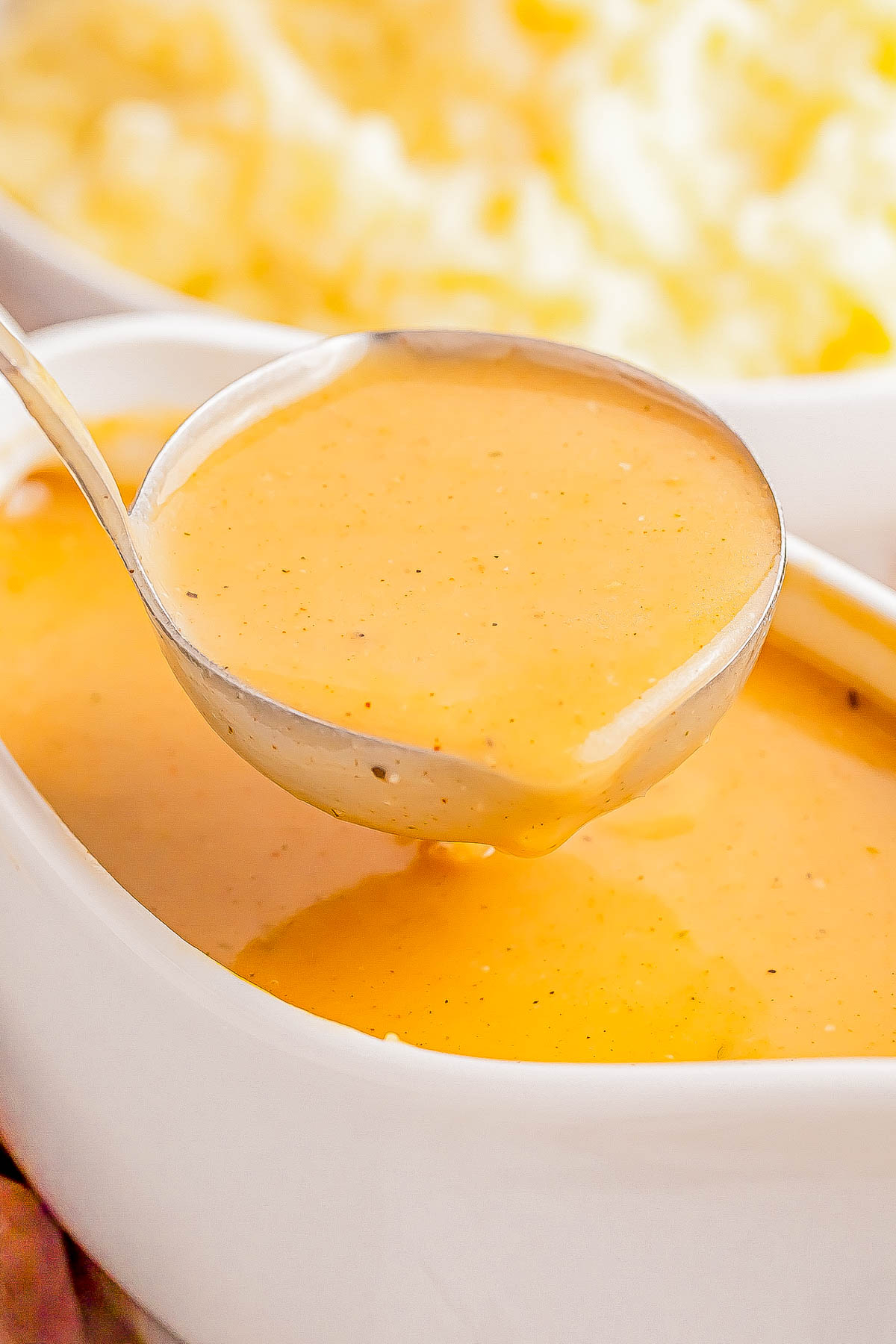 A ladle pouring creamy orange gravy into a white dish.