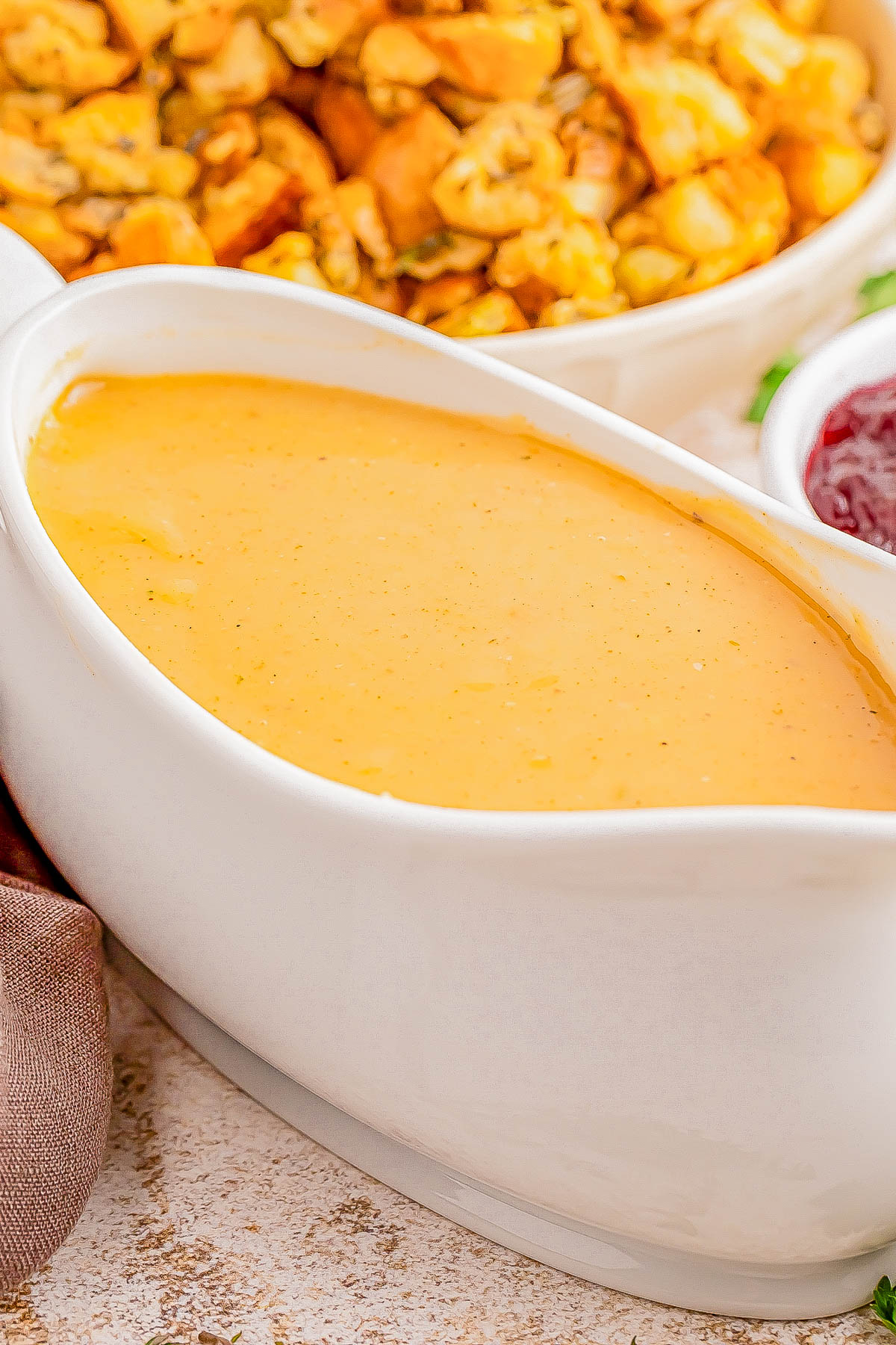 Creamy orange sauce in a white gravy boat with crispy roasted potatoes and cranberry sauce in the background.