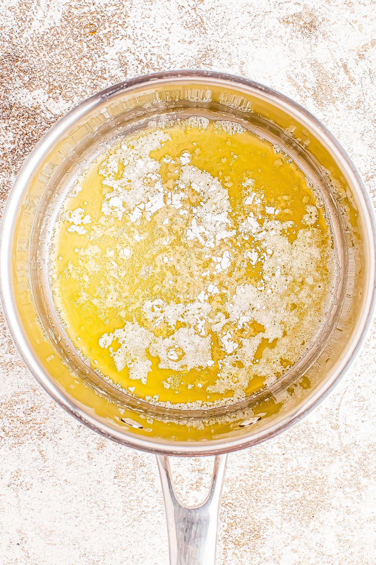 A pot filled with melted butter, showing a layer of frothy bubbles on the surface.