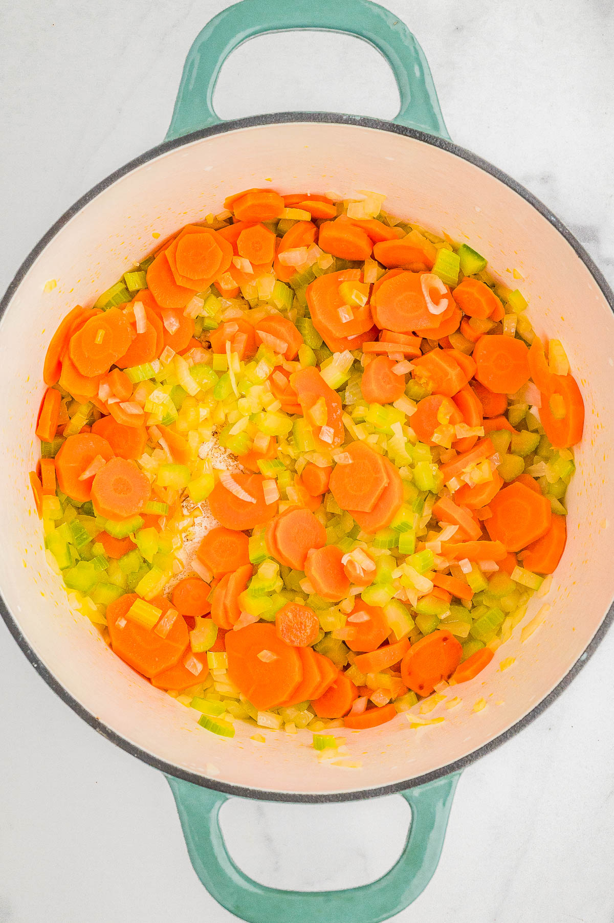 Chopped carrots, celery, and onions in a pot on a marble surface, ready for cooking.