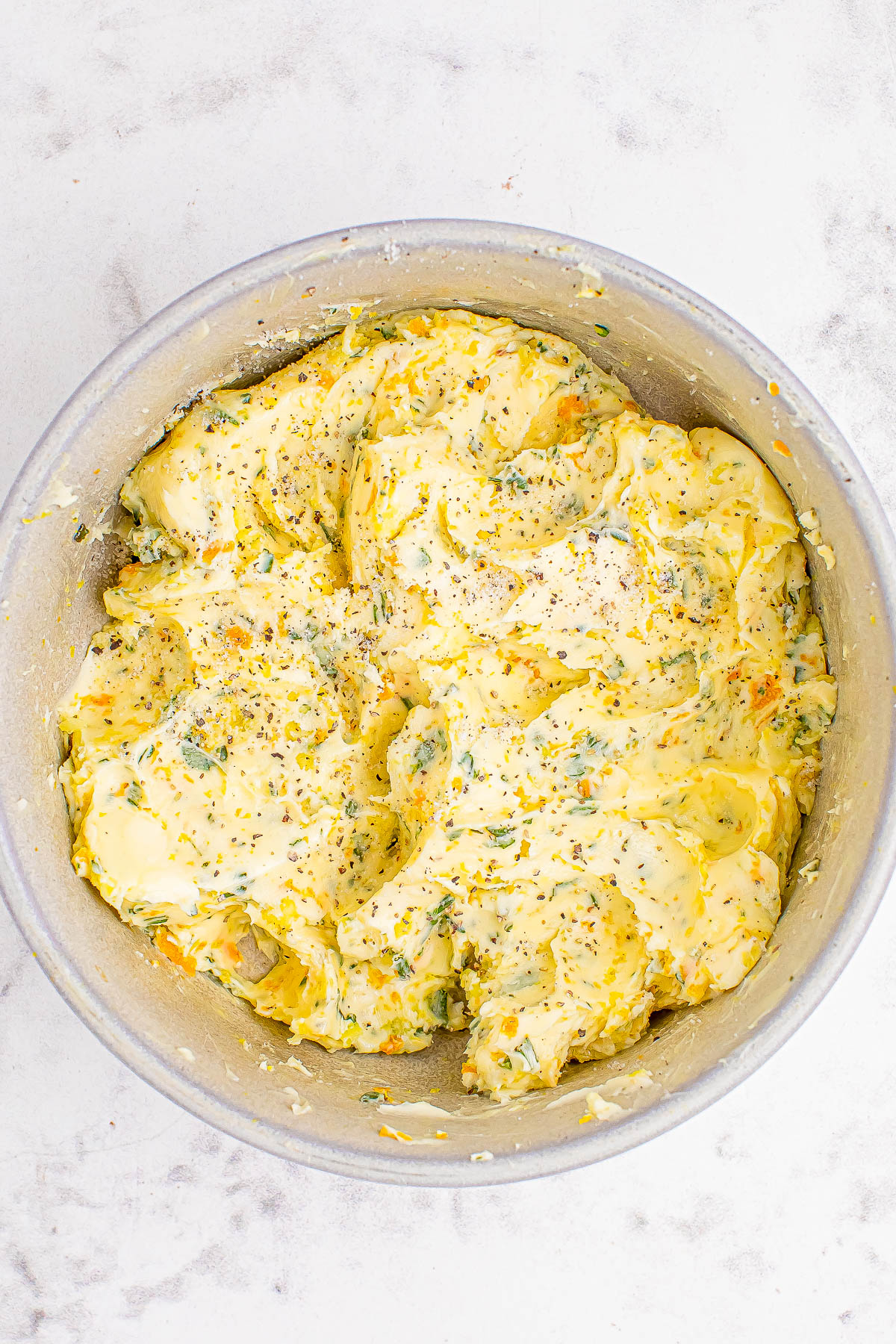 A bowl of seasoned mashed potatoes with herbs, topped with black pepper.