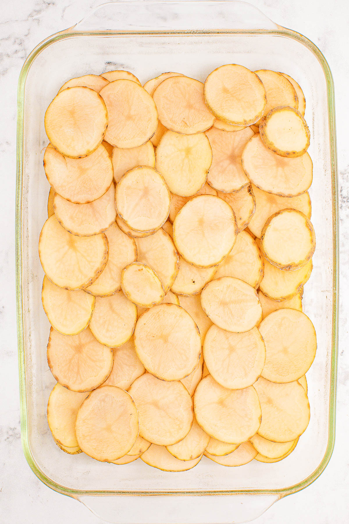 Glass baking dish filled with neatly arranged, evenly sliced raw potatoes.