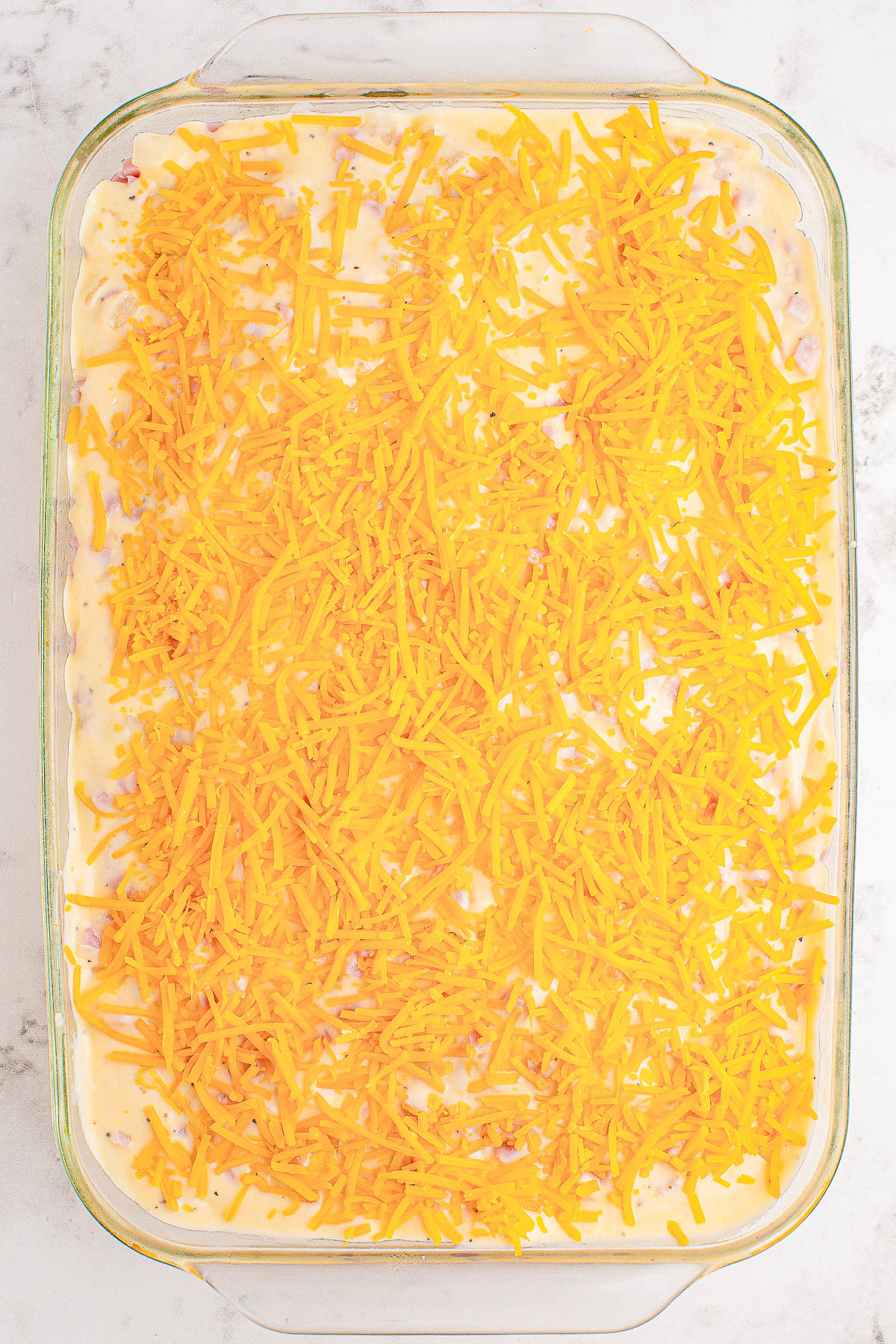 A casserole dish filled with a mixture topped with shredded cheddar cheese.