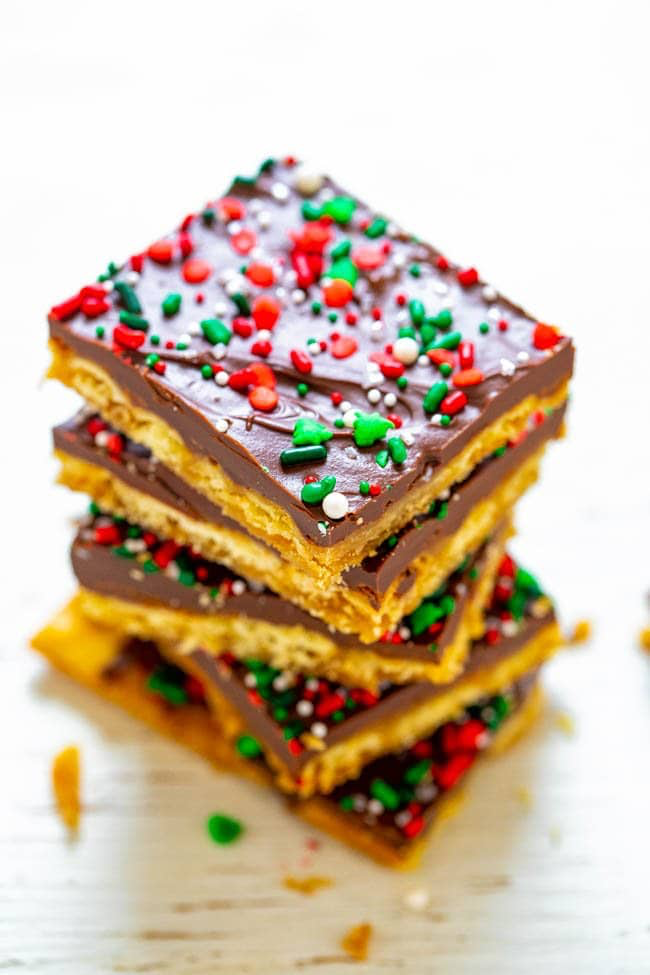 A stack of toffee bars with chocolate topping and red, green, and white sprinkles on a white surface.