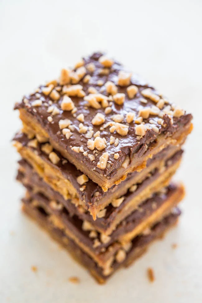 Stack of four chocolate-covered bars topped with chopped nuts on a light background.