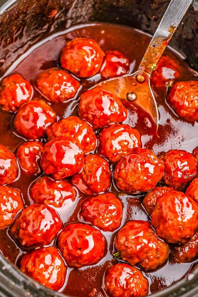 A pot of glazed meatballs in sauce with a spoon.