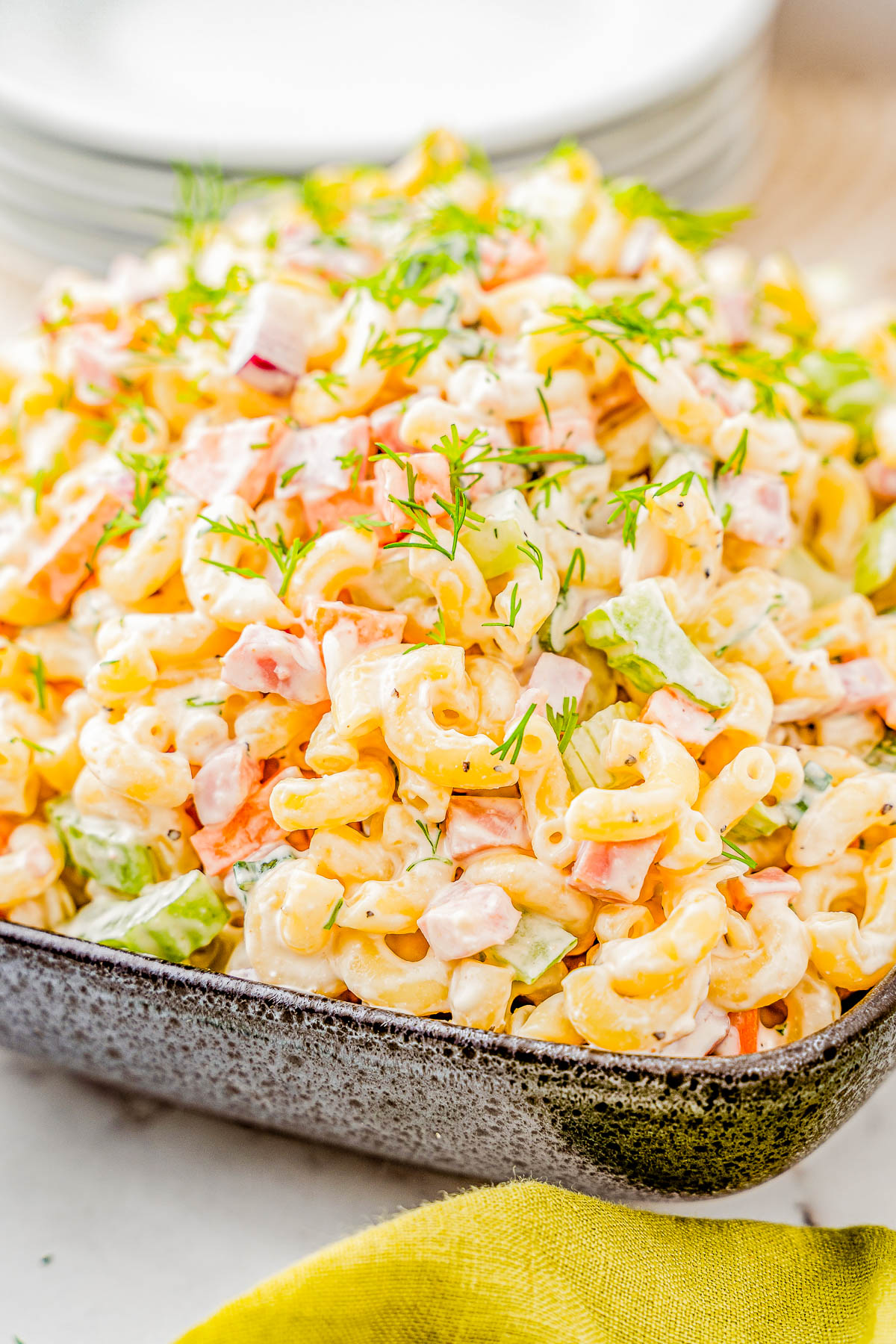 A close-up of a creamy macaroni salad with chopped vegetables and dill in a rectangular dish.