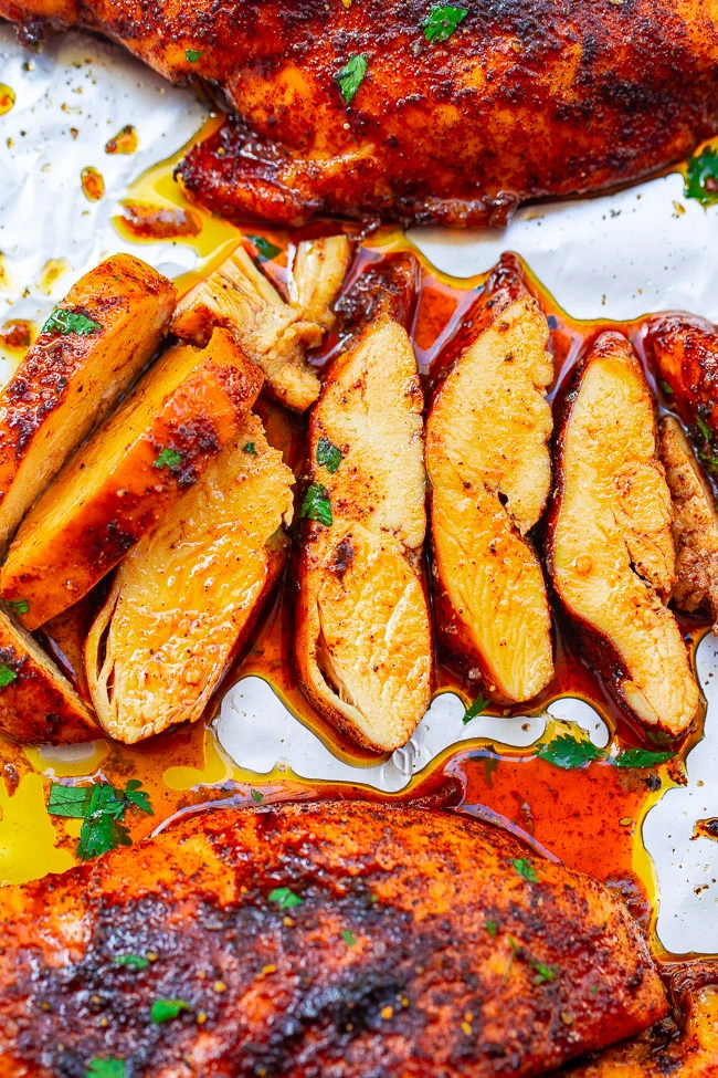 Sliced roasted chicken breast topped with herbs and spices, surrounded by juices and garnished with cilantro on a baking sheet.