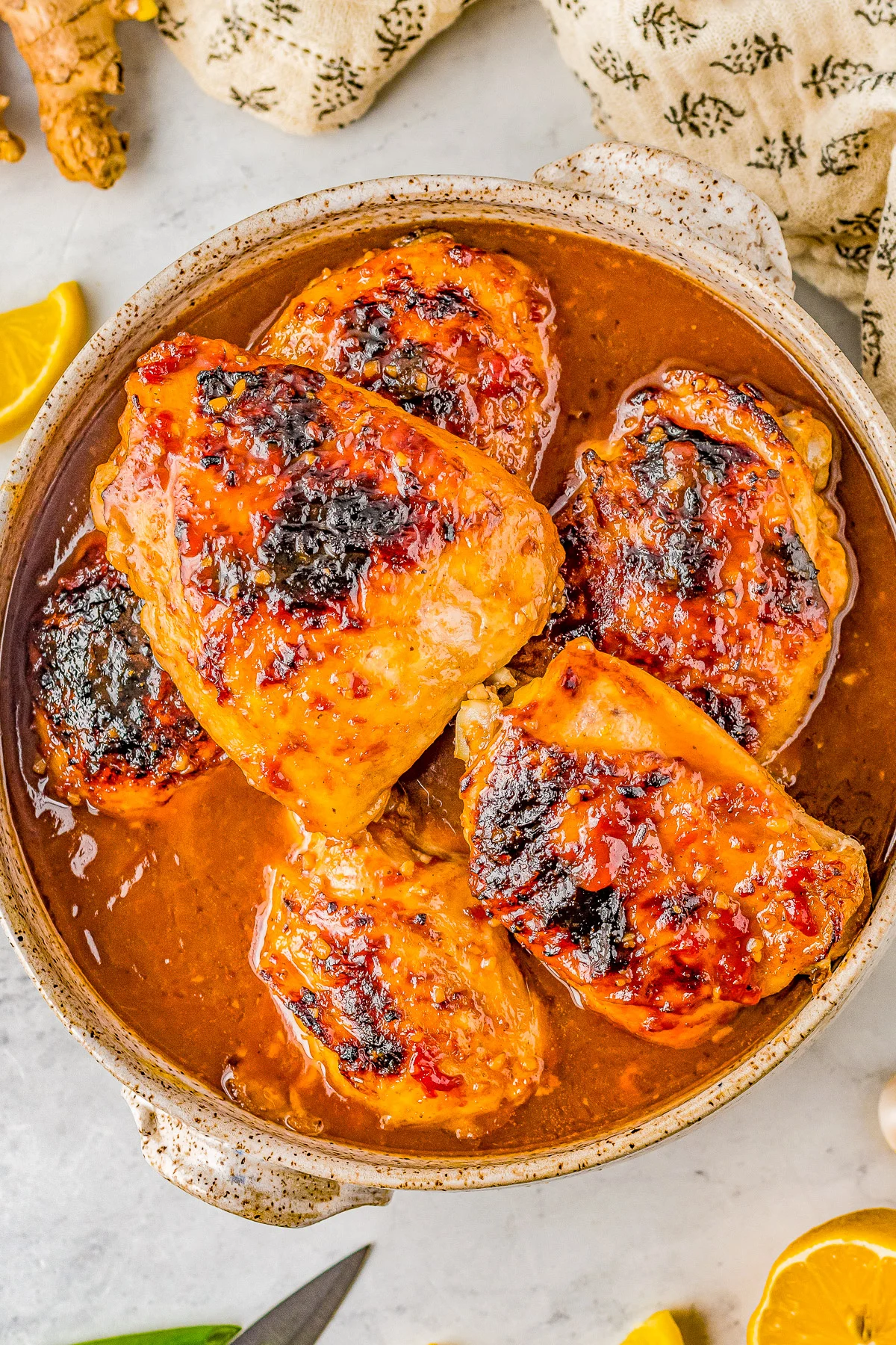 A dish with five pieces of chicken in a reddish-brown sauce, garnished with blackened spots, placed on a light-colored tabletop.