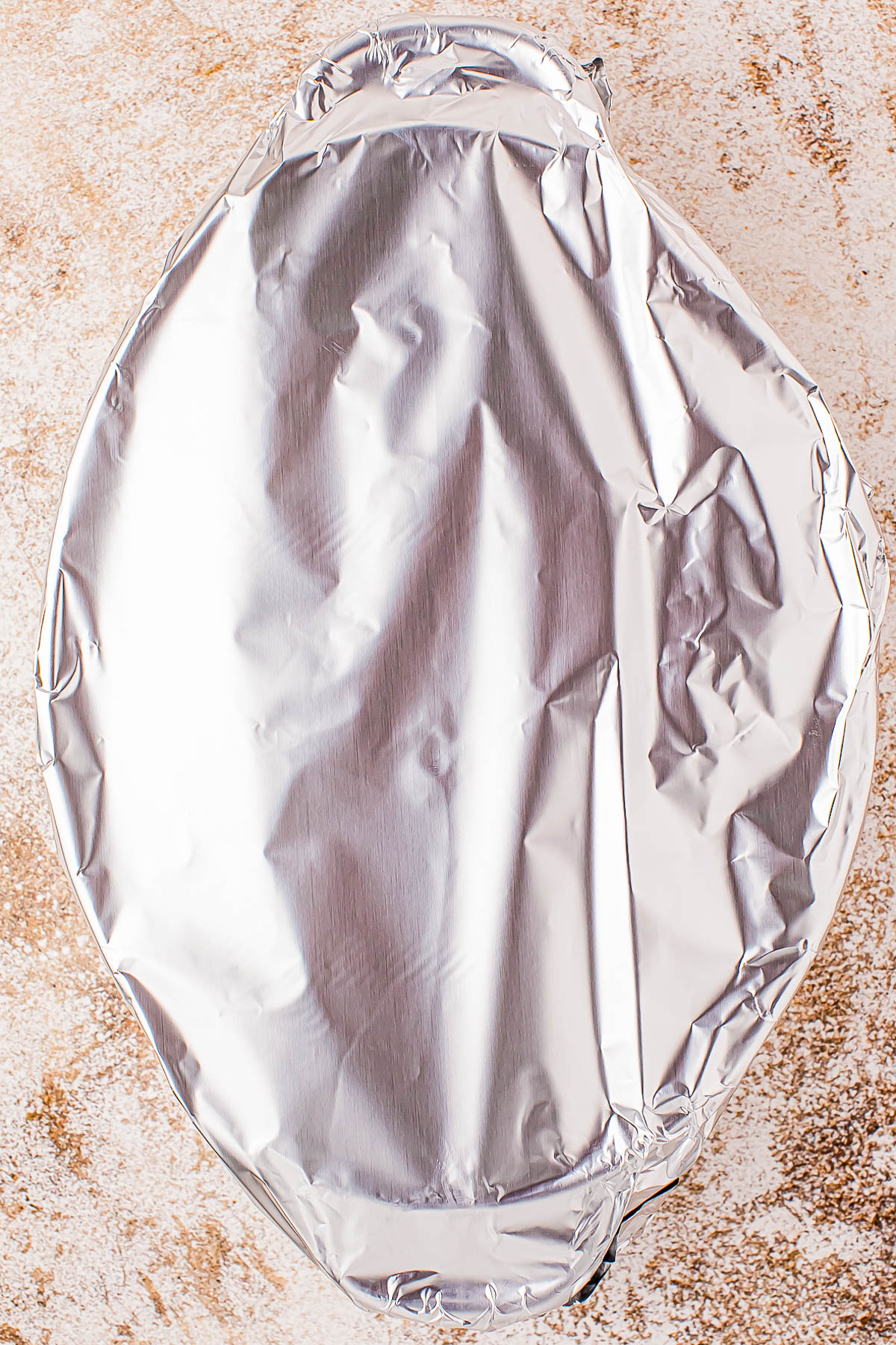 A round dish covered with aluminum foil on a textured surface.