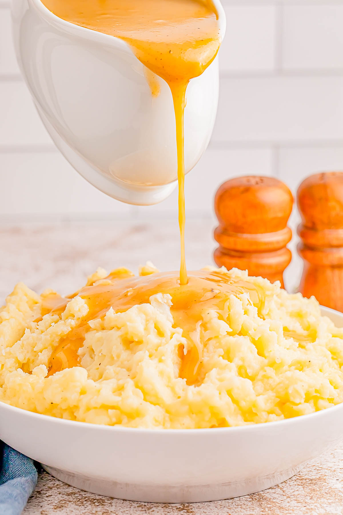 Gravy being poured over a bowl of mashed potatoes, with salt and pepper shakers in the background.