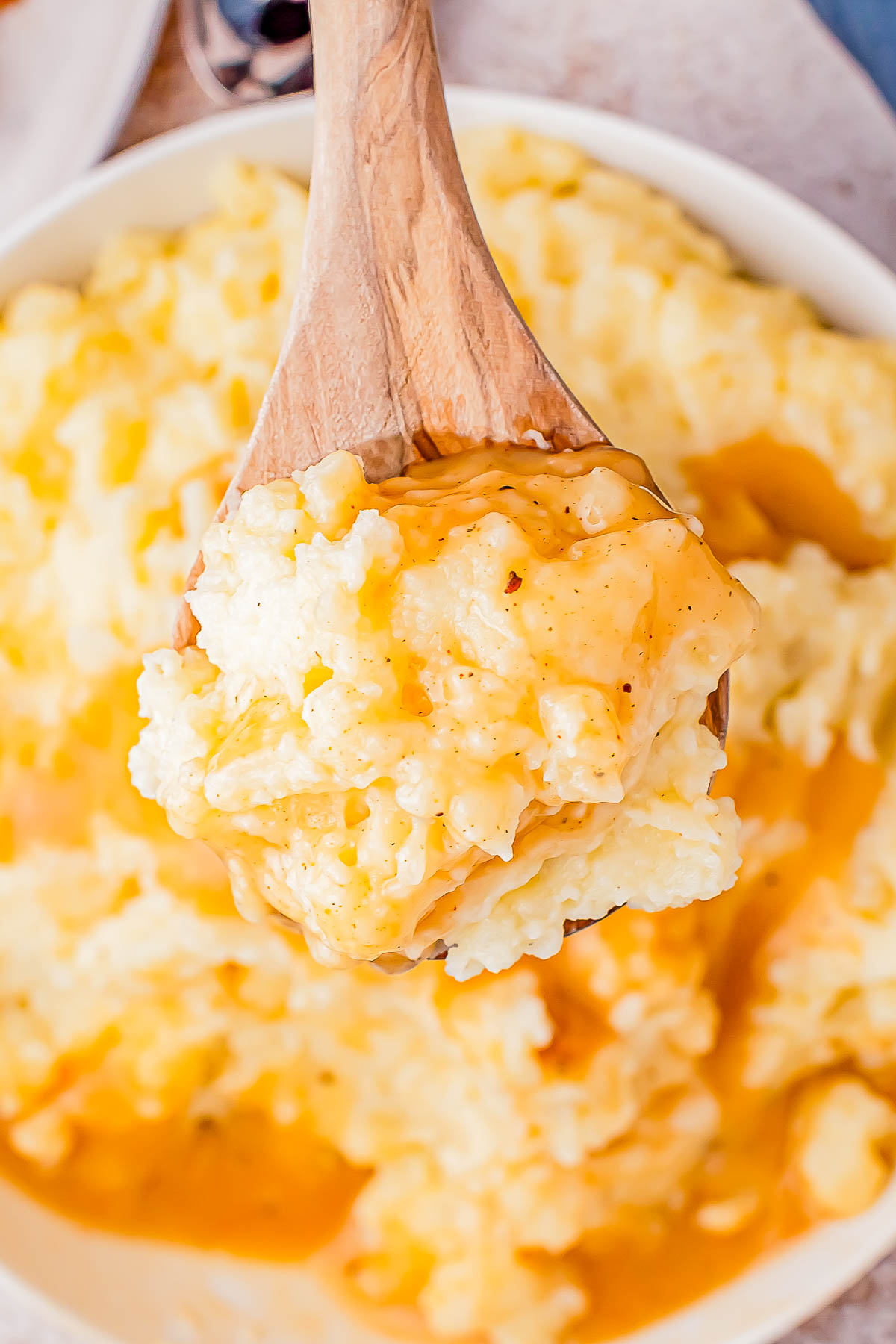 A wooden spoon with a serving of cheesy rice over a bowl of creamy rice.