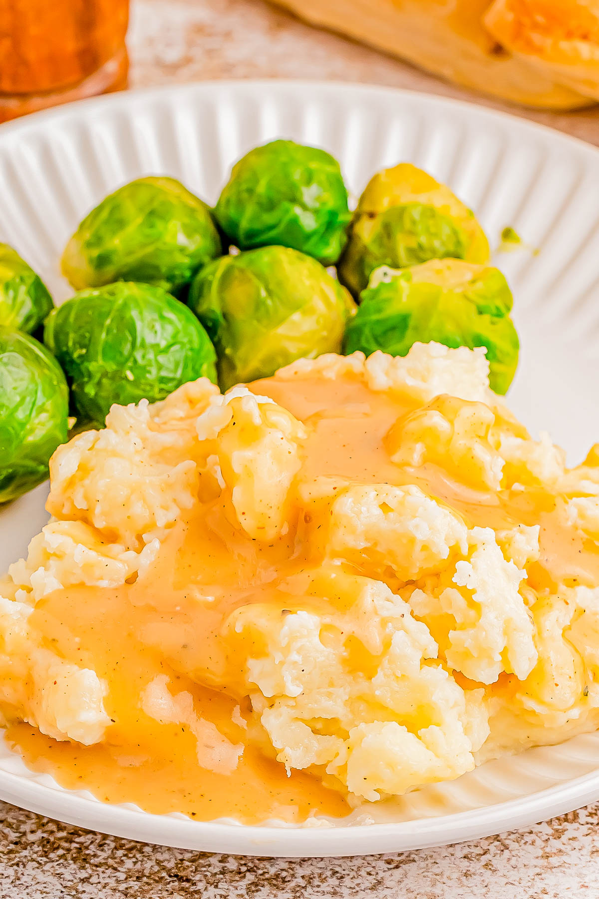 A plate with mashed potatoes topped with gravy and a serving of Brussels sprouts.