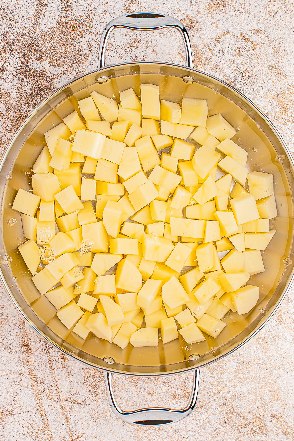 A pot filled with cubed potatoes submerged in water on a textured surface.