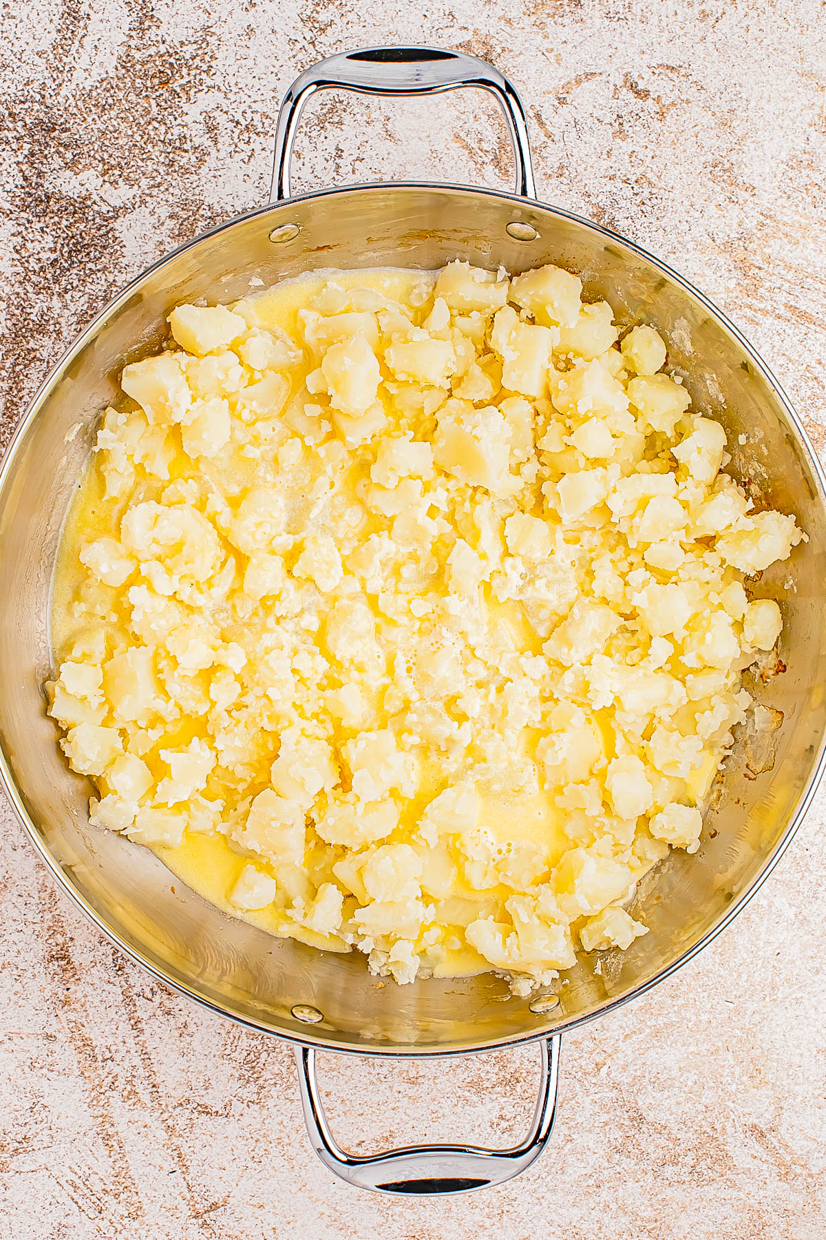 A metal pot filled with mashed potatoes on a textured surface.