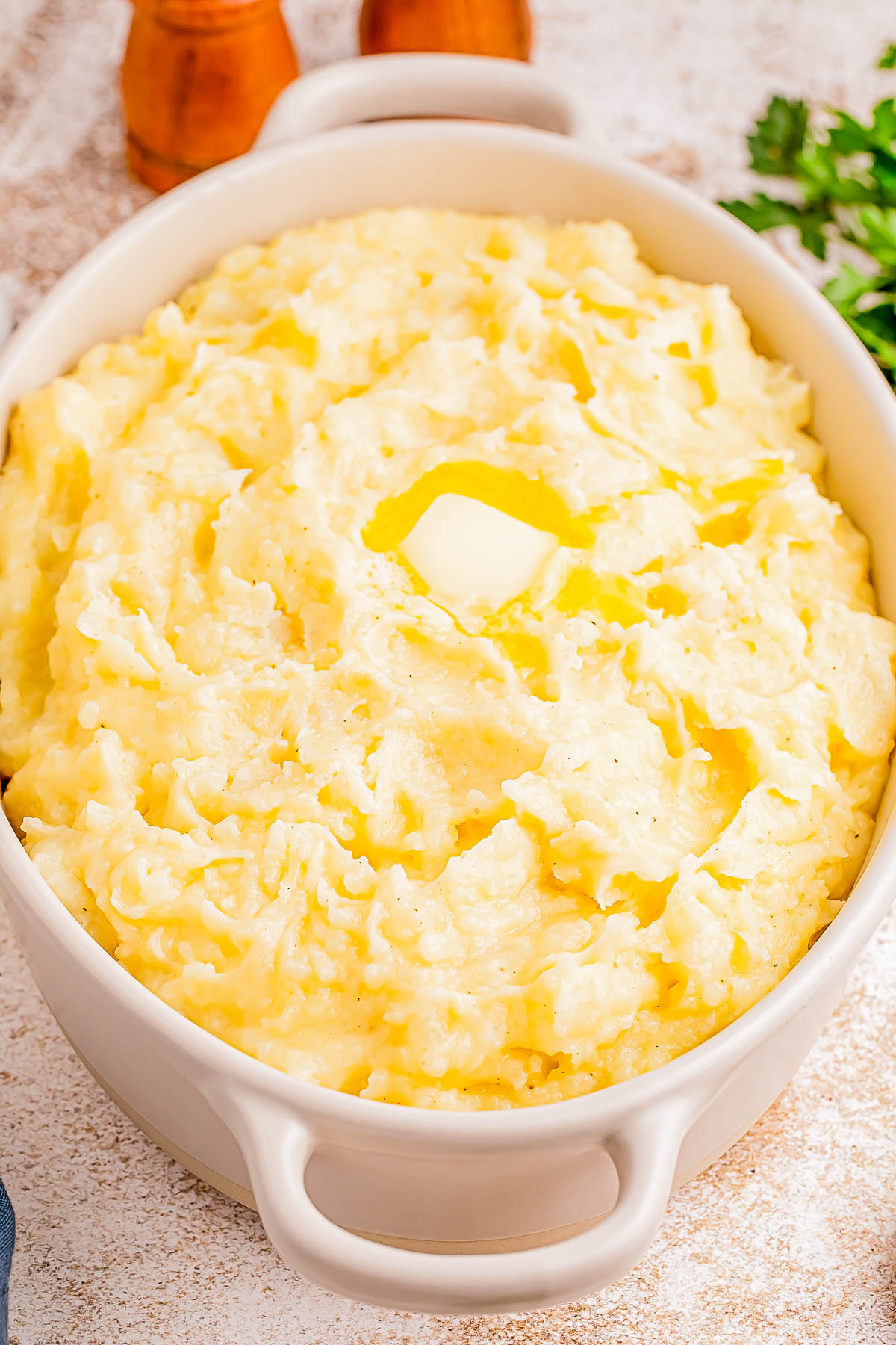 A white ceramic dish filled with mashed potatoes topped with a pat of melting butter.