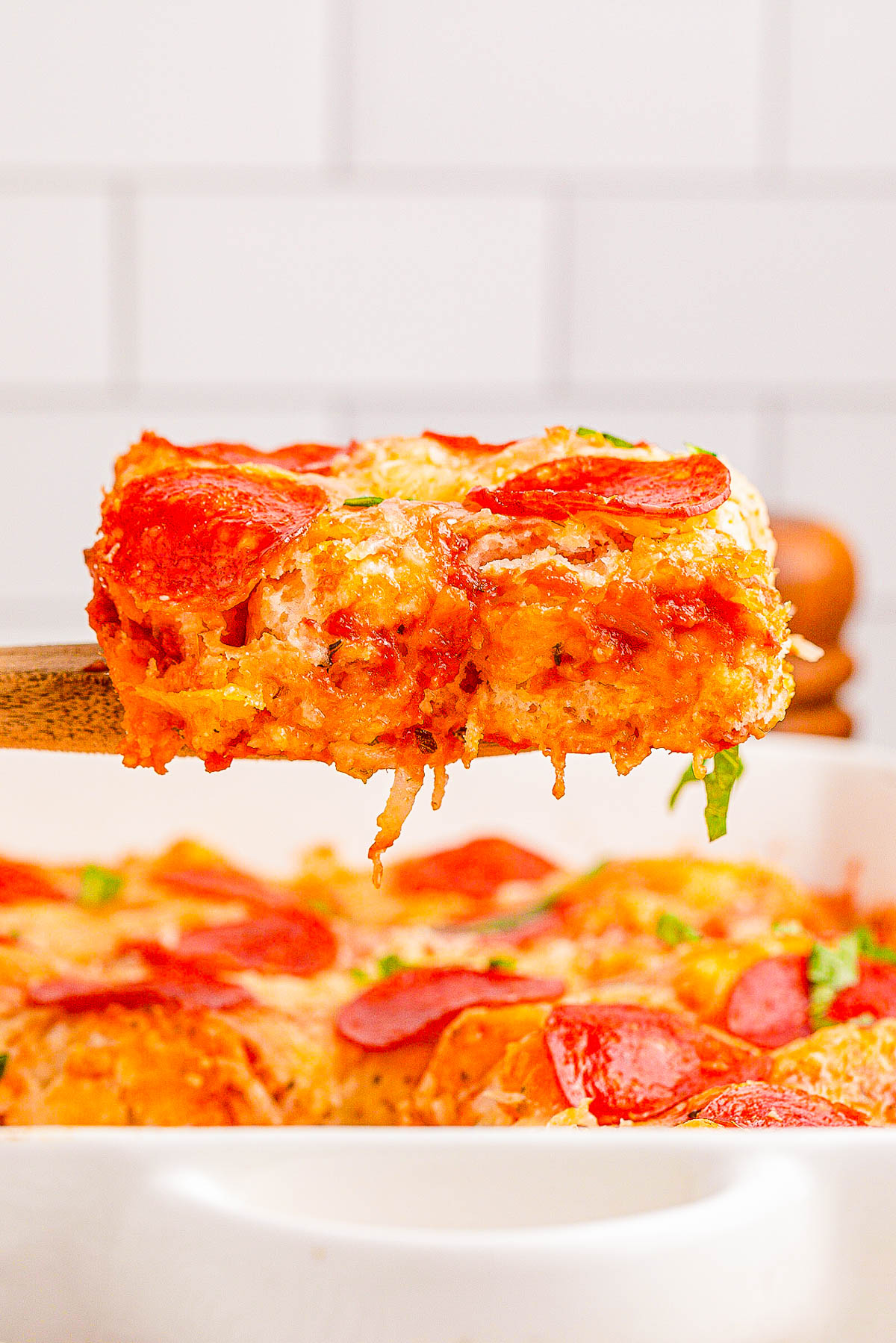 A serving of cheesy pepperoni pizza casserole being lifted from a baking dish.