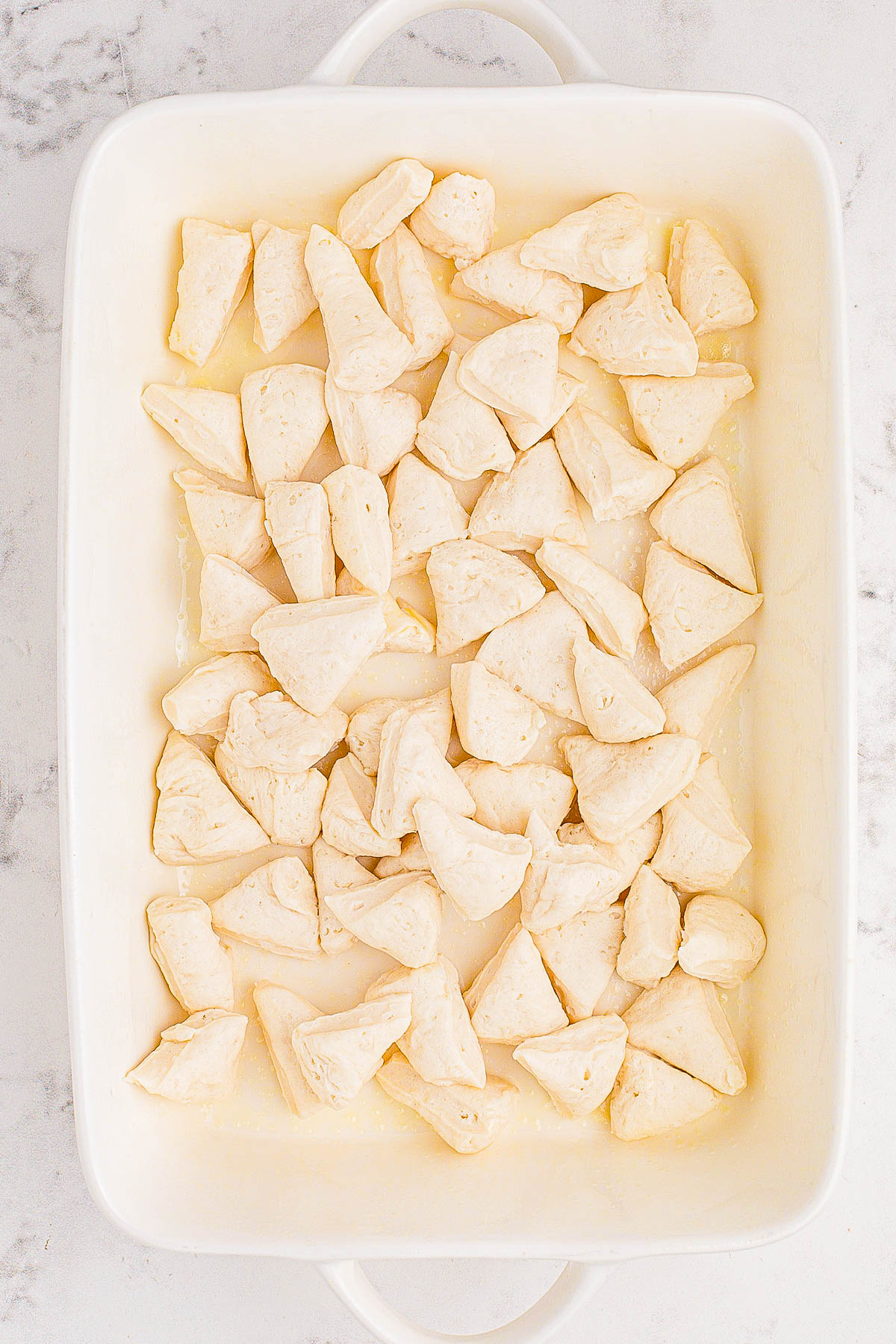 Baking dish filled with unbaked, triangular dough pieces on a marble countertop.