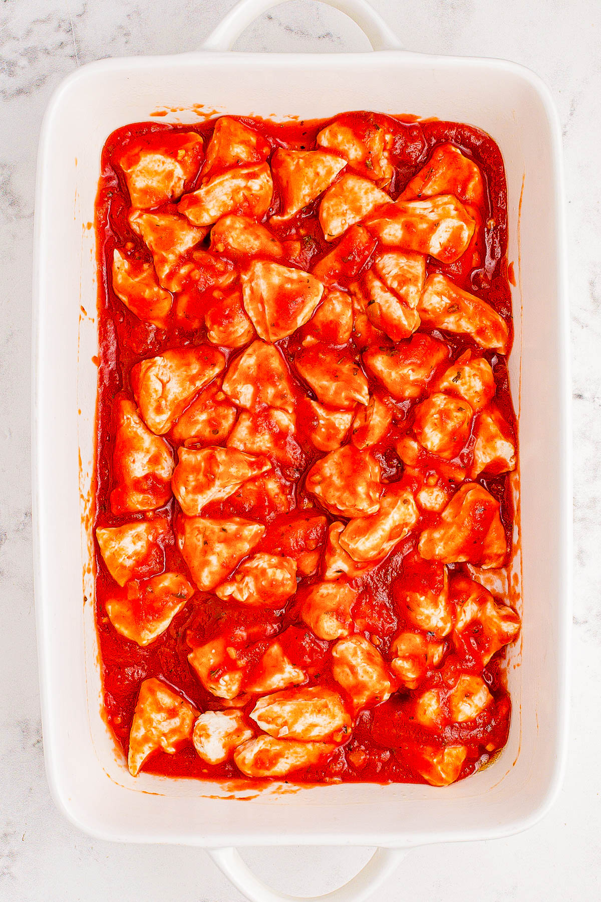 A white baking dish filled with uncooked, cheese-stuffed pasta shells in tomato sauce.